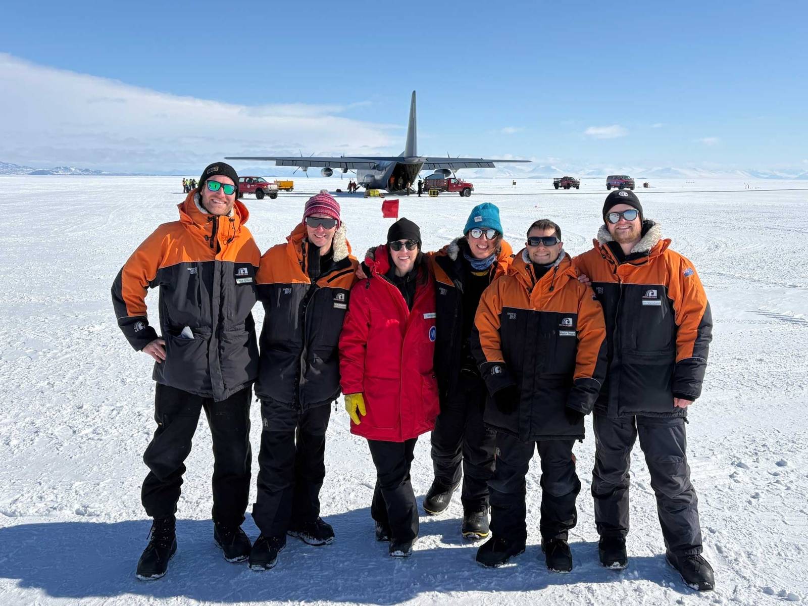 Menschen auf arktischem Eis, im Hintergrund ein Transportflugzeug