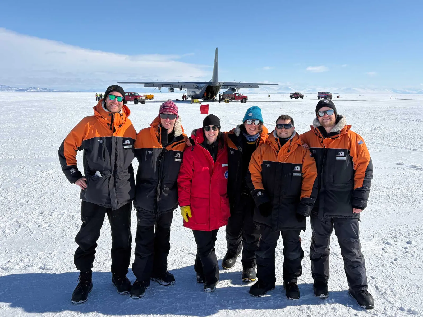 Menschen auf arktischem Eis, im Hintergrund ein Transportflugzeug