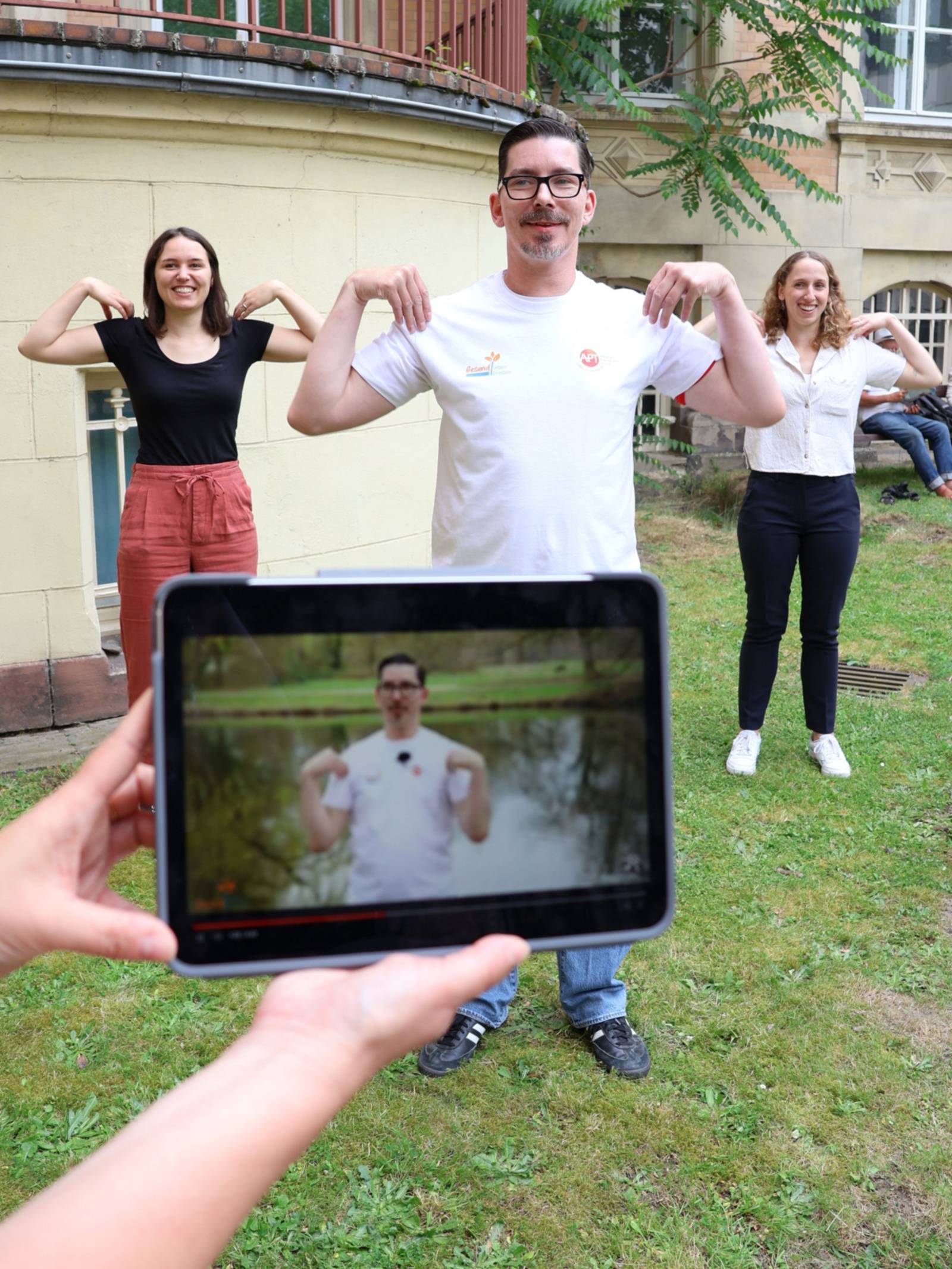 Drei Personen bei sportlicher Betätigung. Die Anleitung dazu kommt aus einer App auf einem Tablet.