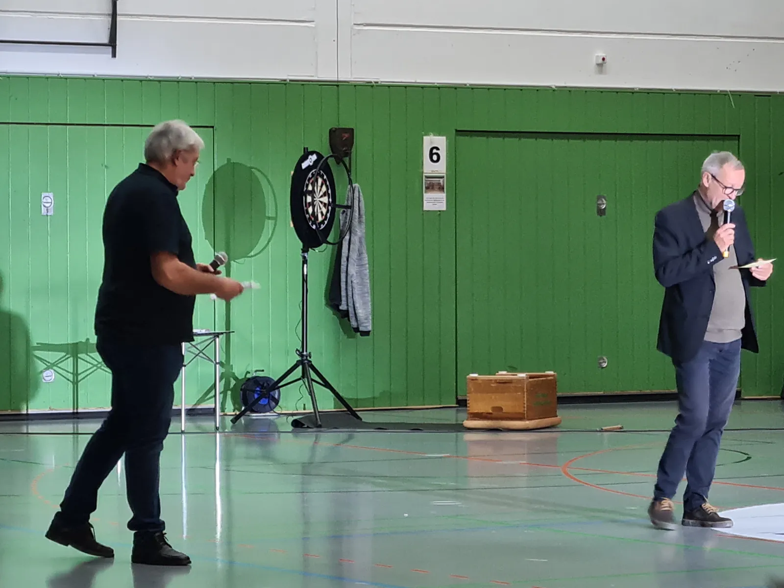 Auf dem Bild sind zwei M&auml;nner zu sehen, die in einer Turnhalle moderieren.