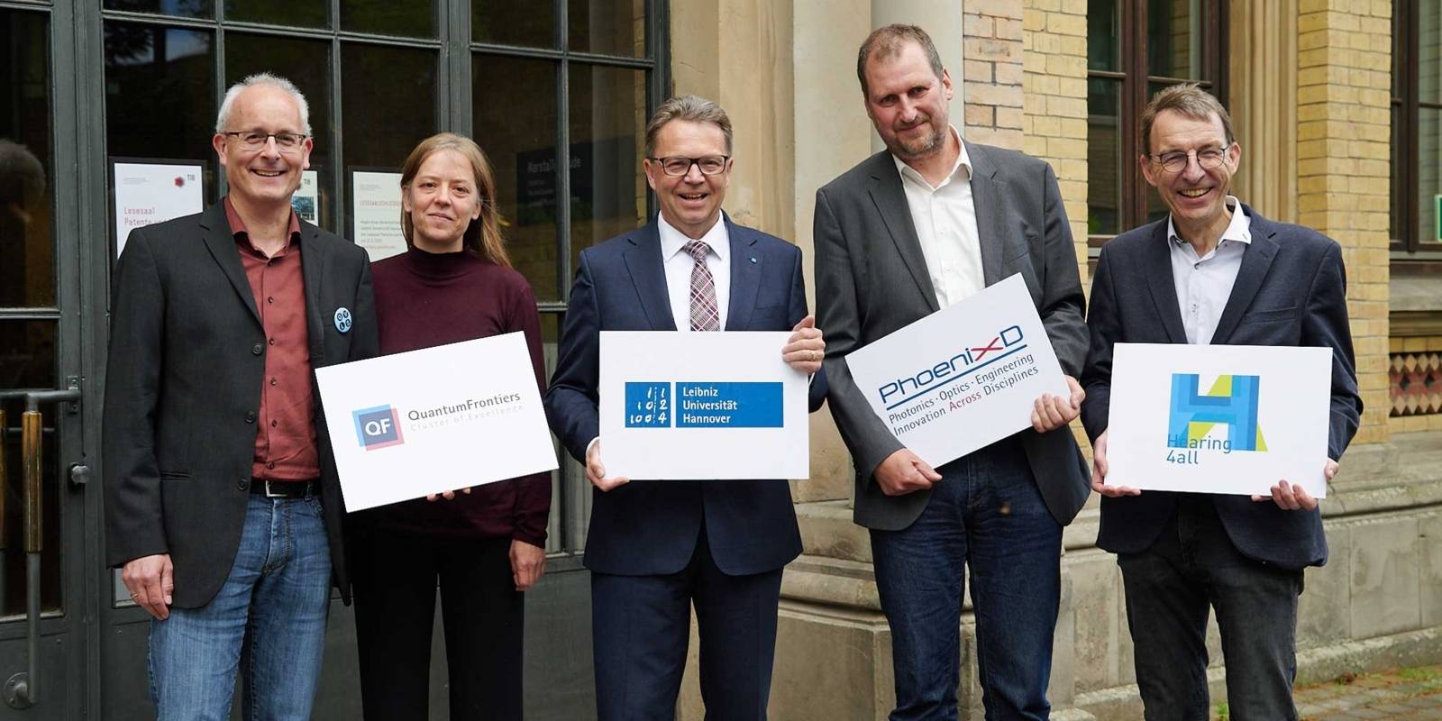 Eine Frau und vier M&auml;nner halten Tafeln mit Logos in den H&auml;nden.