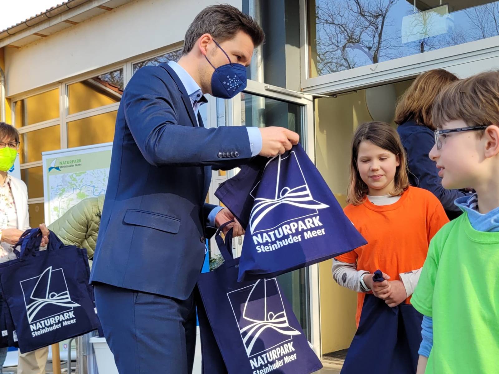 Ein Mann übergibt Stoffbeutel samt Inhalt an Kinder.