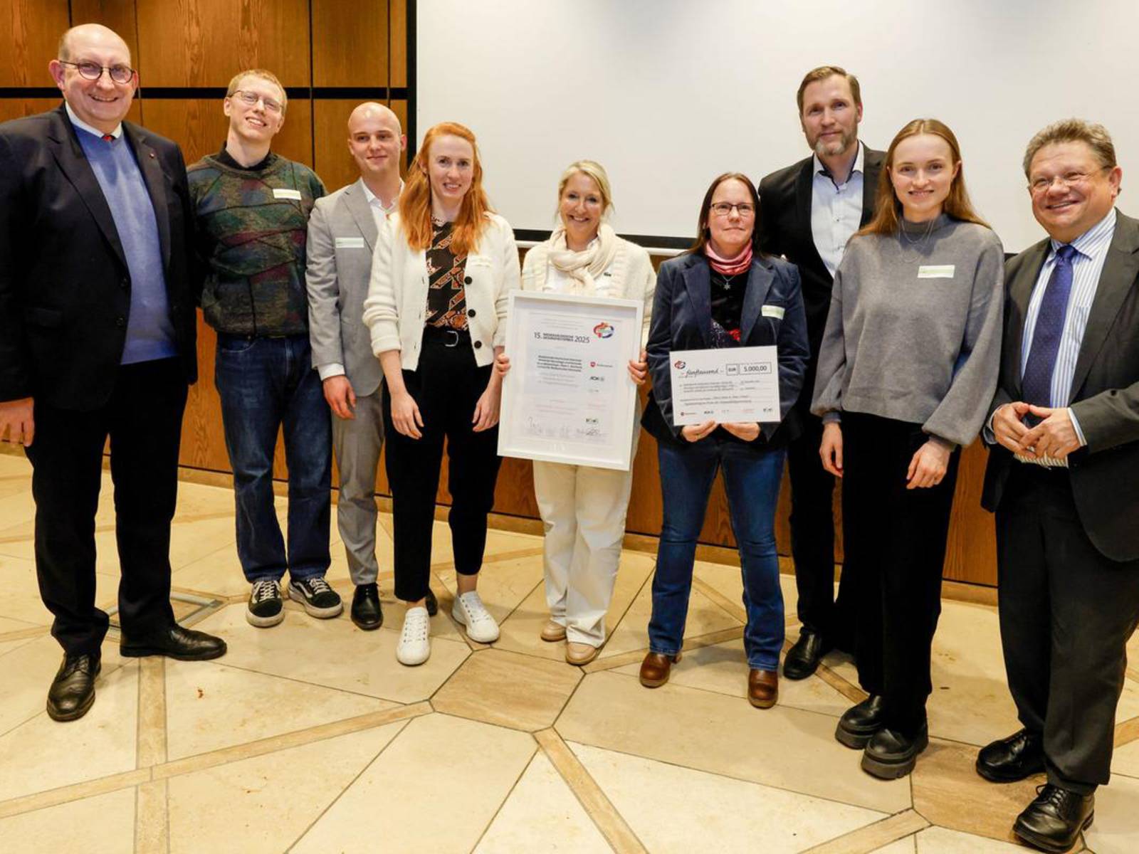 Eine Menschengruppe mit Urkunde auf einer Bühne.