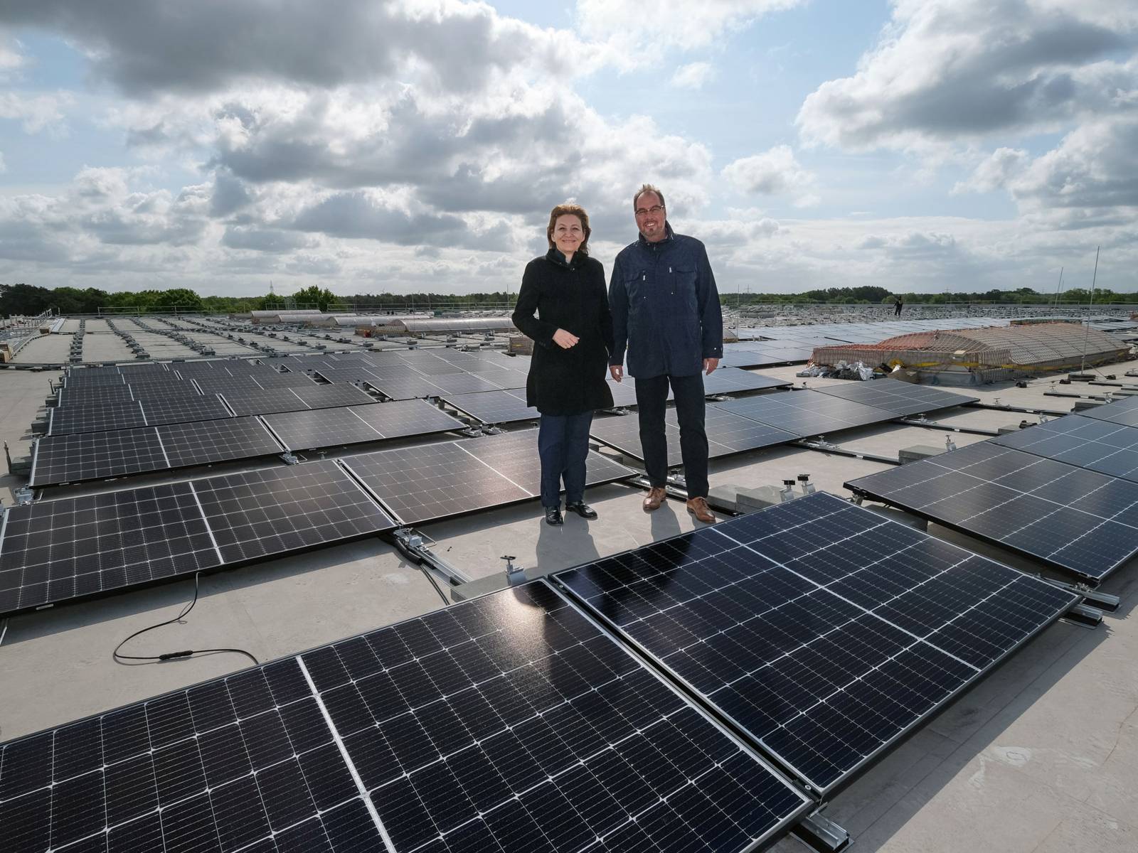 Eine Frau und ein Mann stehen auf einem großen Flachdach zwischen Solarzellen.