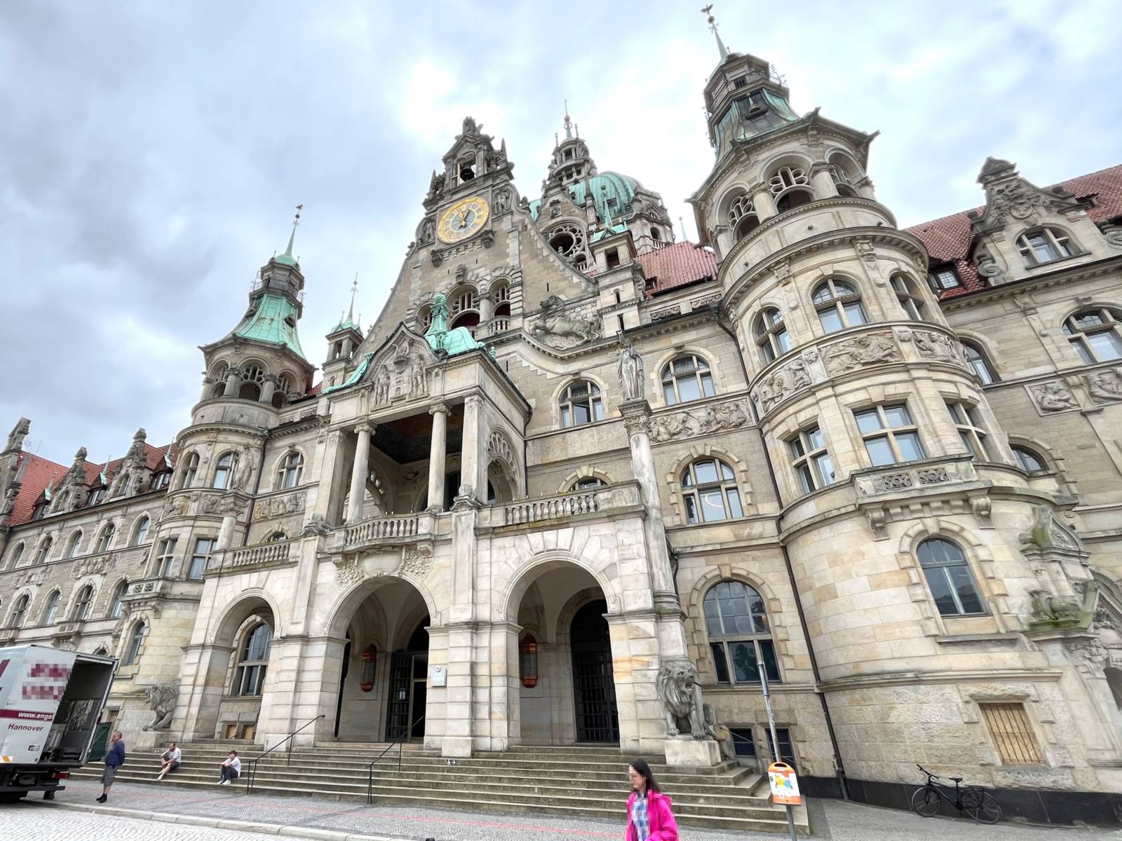 Ein altes, schlossähnliches Gebäude im wilhelminischen Stil mit Verzierungen. Über drei Eingangsbögen ein teilweise überdachter Balkon, darüber eine Uhr und ein Fenster mit einer Glocke.