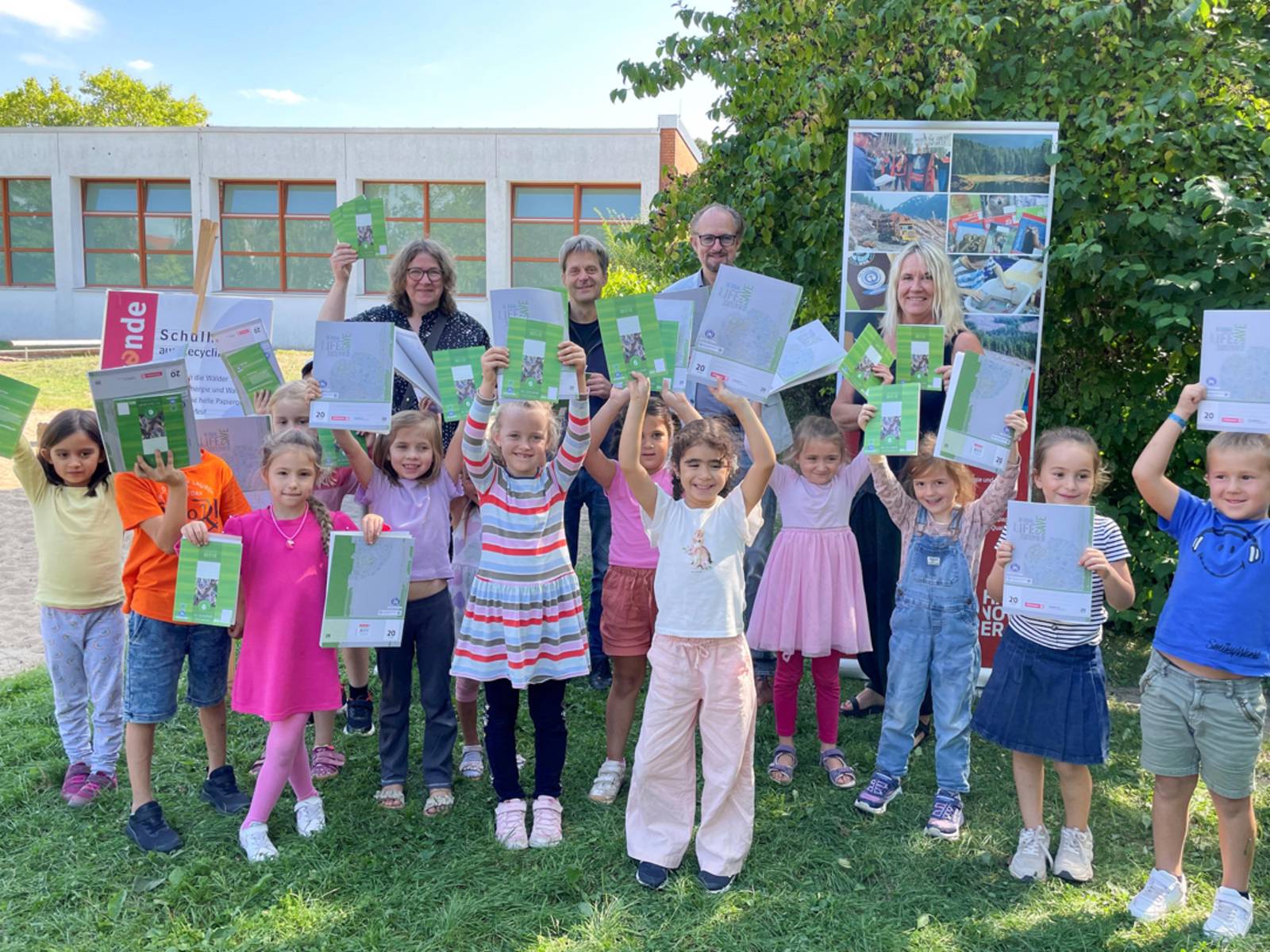 Drei Erwachsene mit Kindern, die Schulhefte nach oben halten.