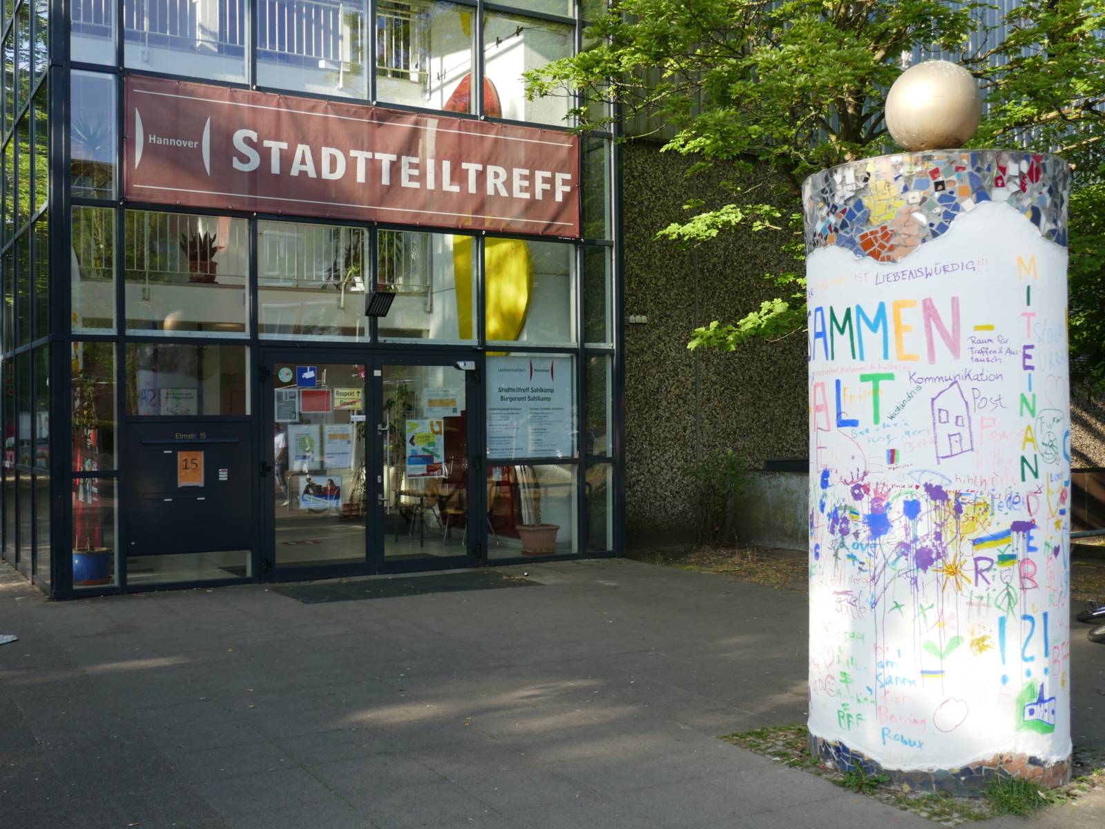 Vor dem Eingang des Stadtteiltreffs steht eine hohe bunt angemalte Litfaßsäule. Alle sind im Stadtteiltreff Willkommen!