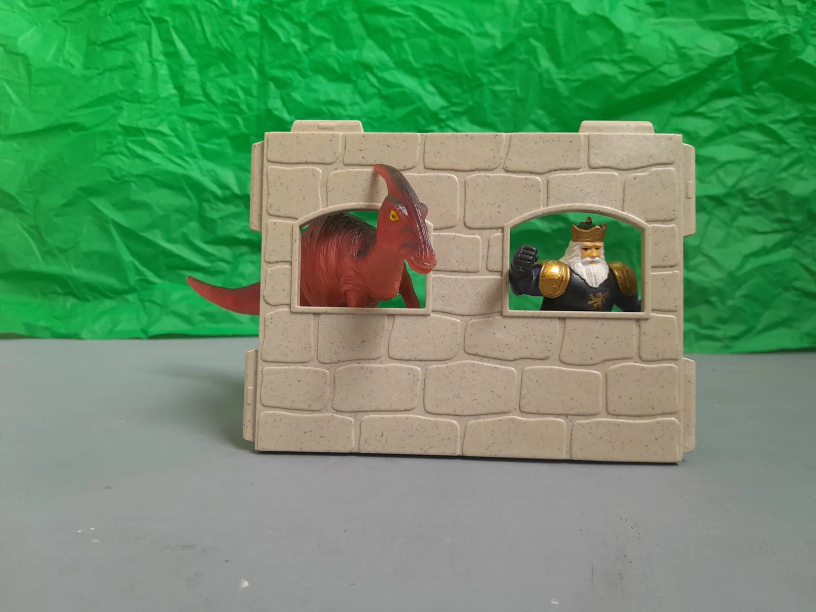 Ein  Spielzeug Dino und ein König schauen durch zwei Fenster in einer Wand.