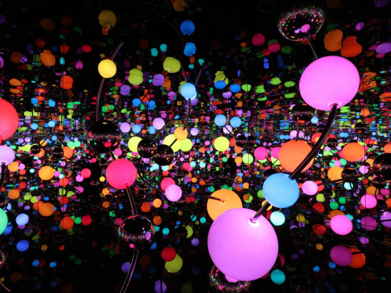 Zu sehen ist eine Lichtinstallation von Yayoi Kusama. Bunt leuchtende Kungeln in unterschiedlichen Farben sind in einem dunklen aber spiegelnden Raum verteilt.