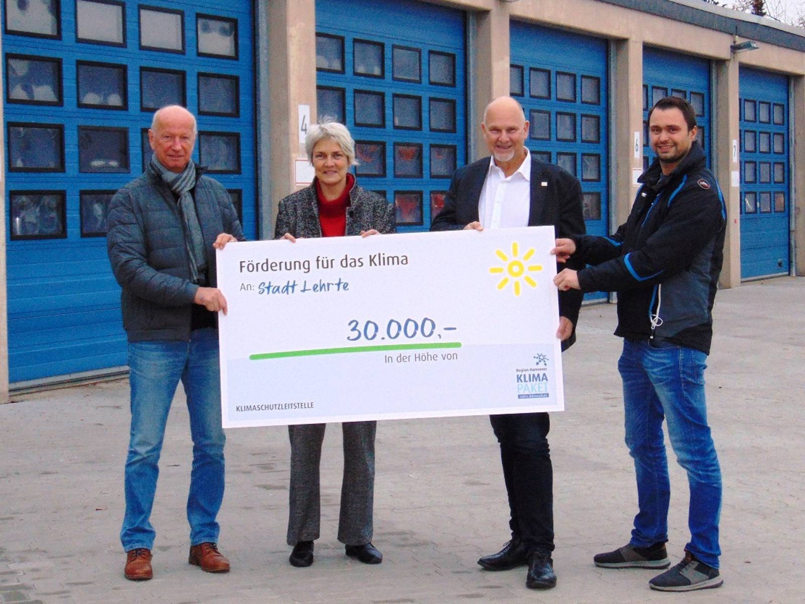 Vier Personen mit einem symbolischen Scheck über 30.000 Euro vor den Toren einer Werkshalle