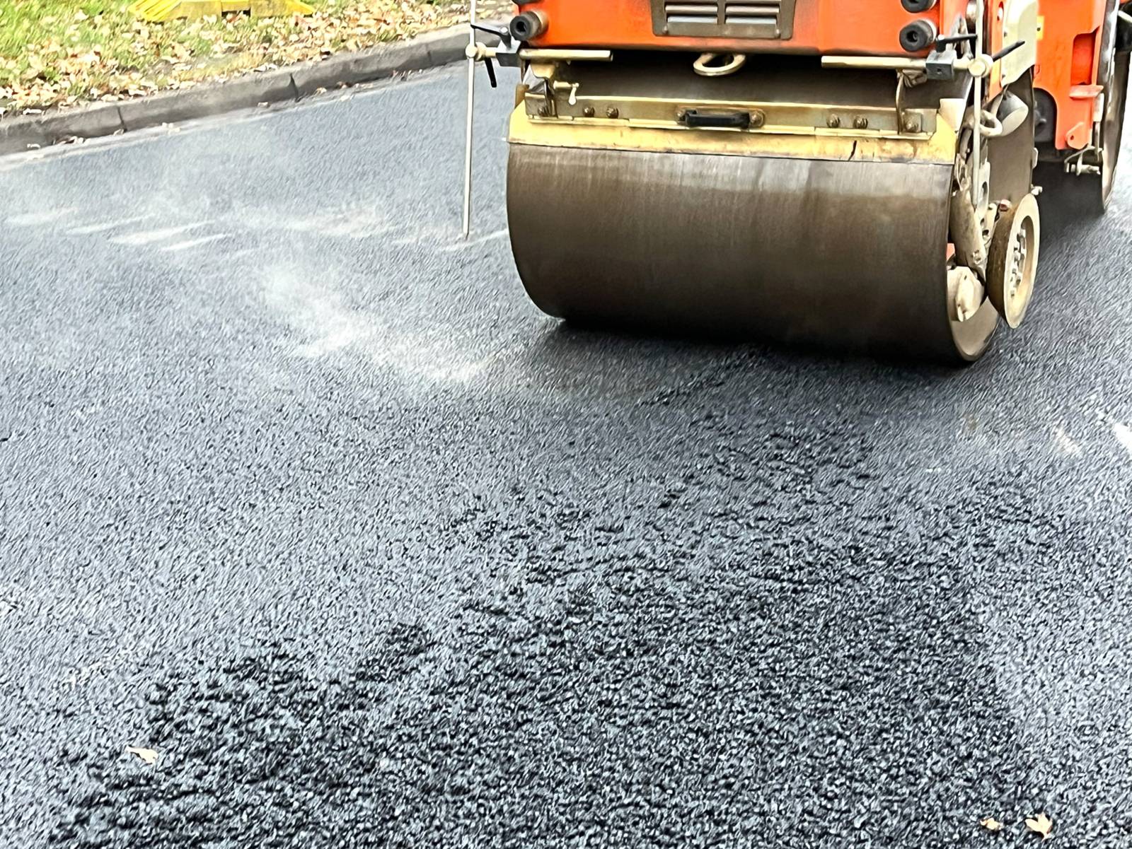 Auf einer dampfenden schwarzen Asphaltschickt rollt eine große Walze eines Fahrzeugs.