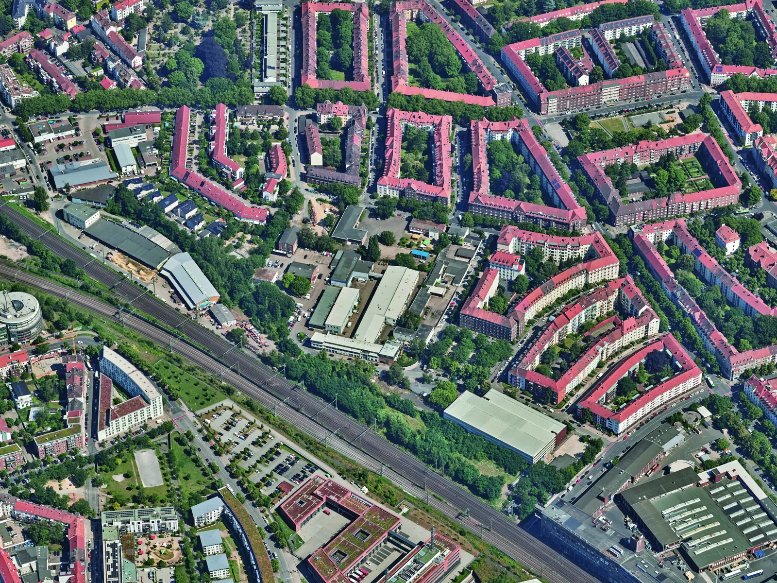 Luftbild eines Quartiers mit Wohnhäusern, weiteren Gebäuden und einer Bahntrasse