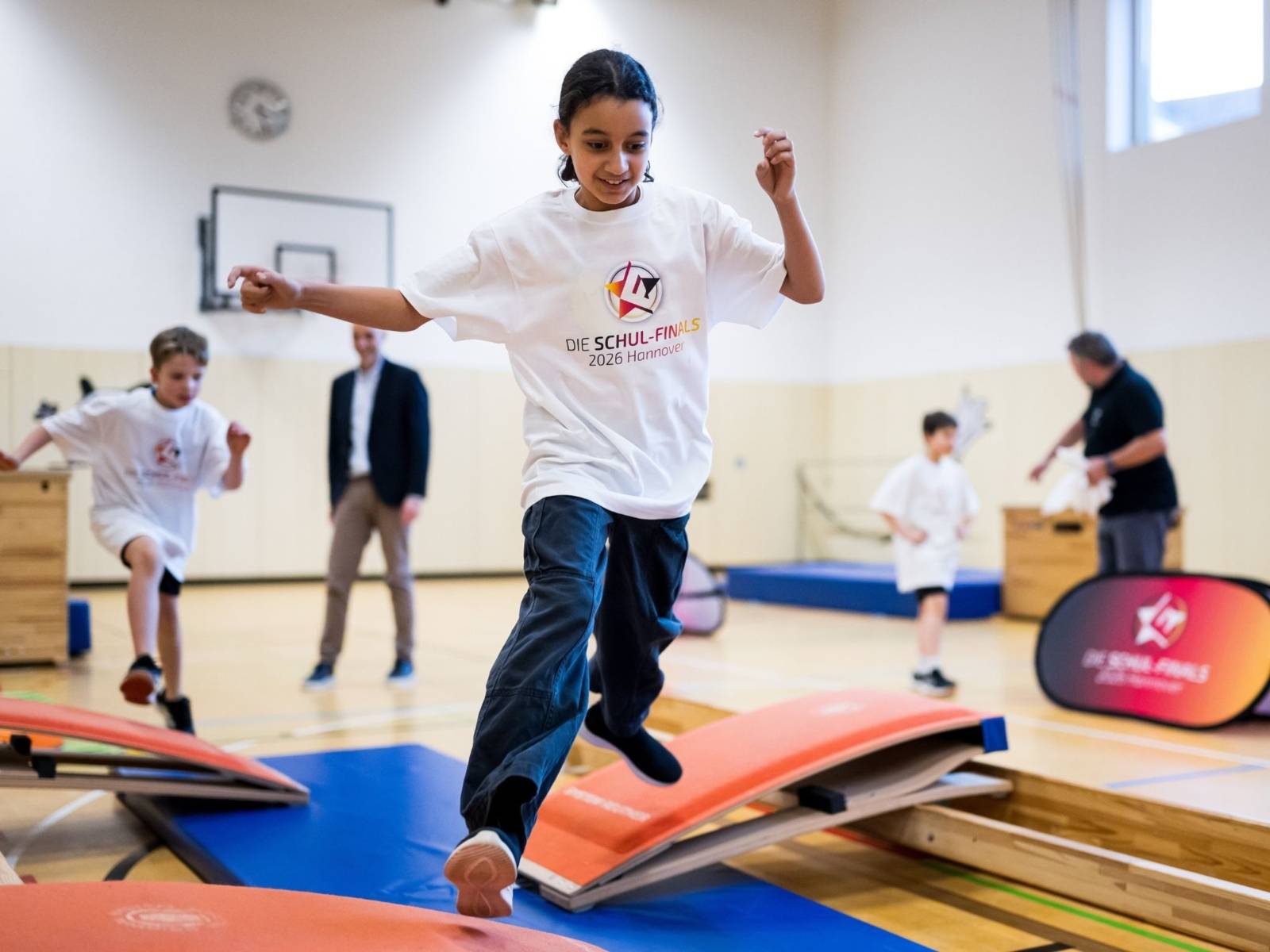 Ein Kind springt in einer Turnhalle auf einem Parkour.