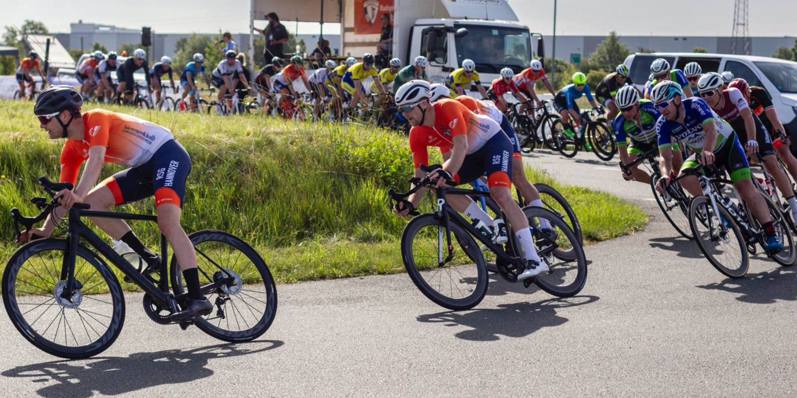 Rennradfahrer fahren auf einer Stra&szlig;e hintereinander durch eine Kurve.