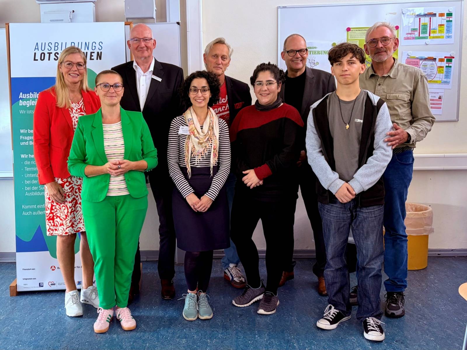 Auf dem Foto stehen mehrere Menschen, darunter Erwachsene und Schüler*innen, die in die Kamera schauen.