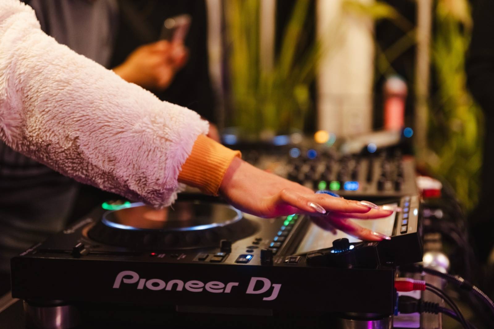 Ein DJ-Pult. Eine Hand mit langen Fingernägeln bedient es.