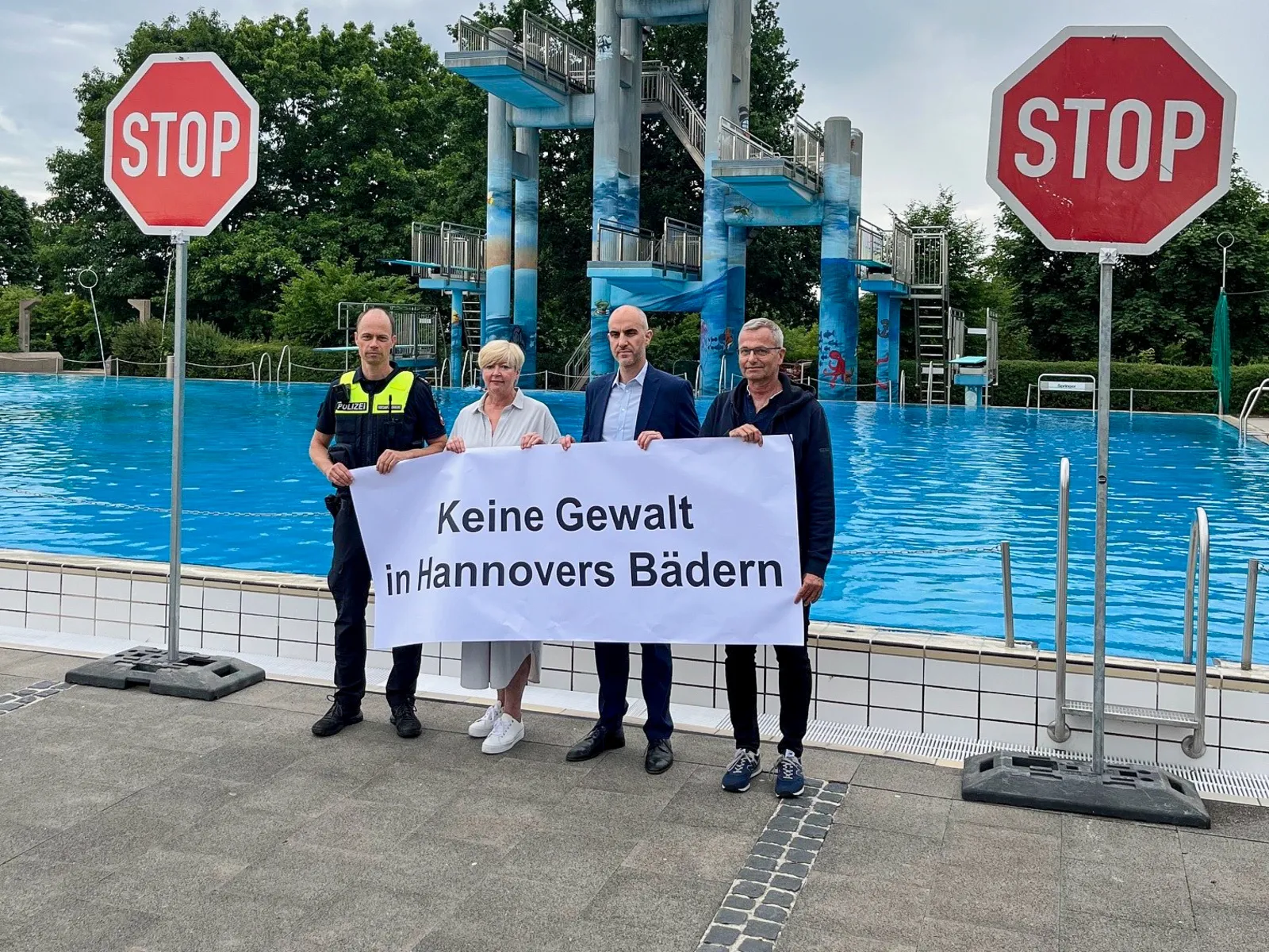 Vier Personen in einem Schwimmbad. Daneben zwei "Stop"Schilder.
