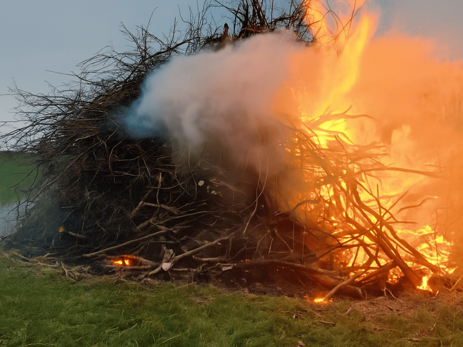 Zu einem großen Haufen aufgeschichtete dicke und dünnere Äste auf einem Feld, die brennen.