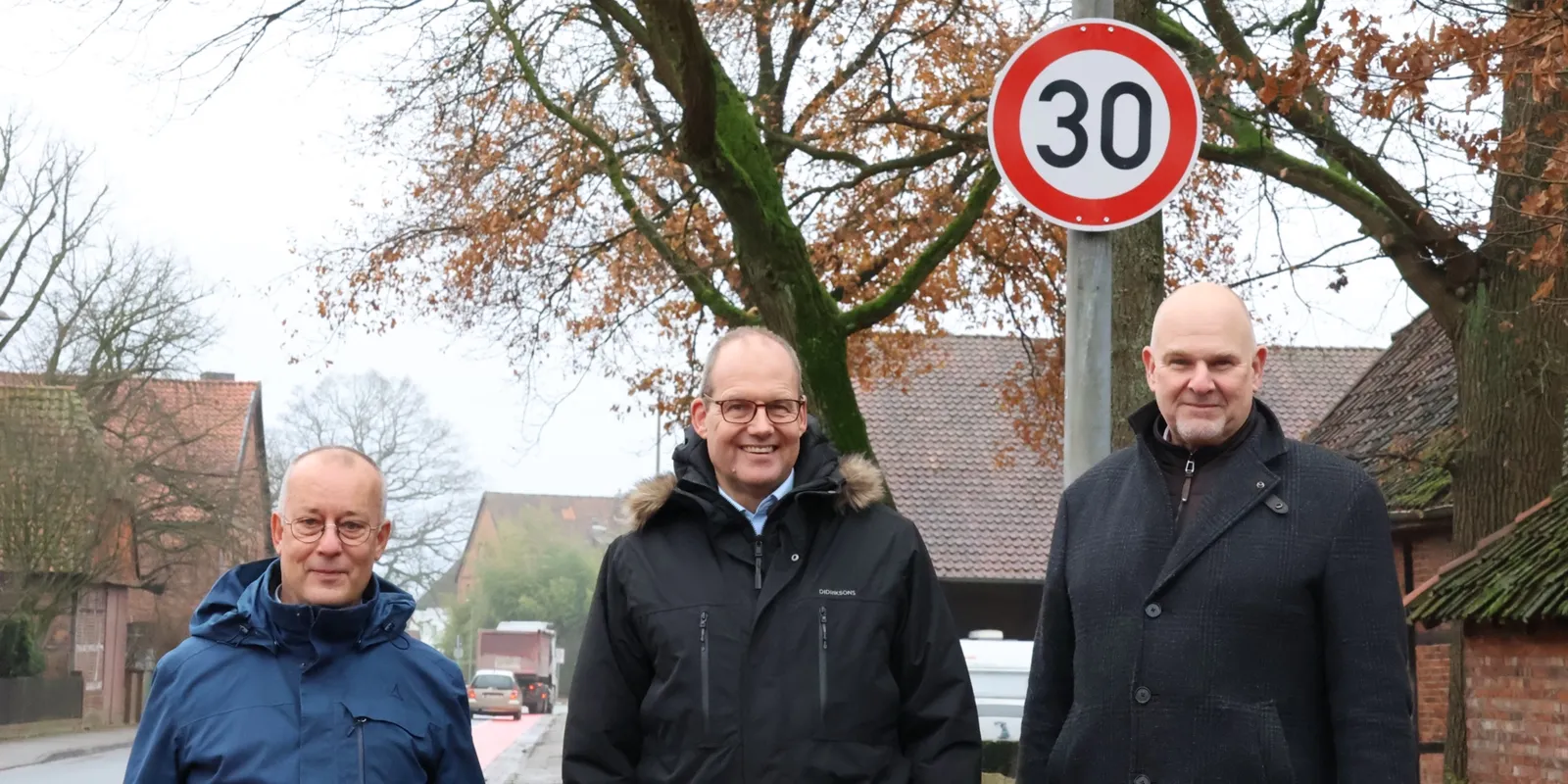 Drei M&auml;nner stehen auf dem B&uuml;rgersteig neben einer Stra&szlig;e, direkt hinter ihnen ist ein Schild "Tempo 30".