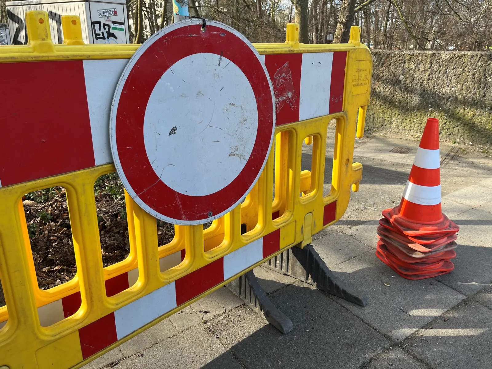 Eine gelbe Absperrung mit einem Schild aus einem weißen Kreis, rot umrandet, Baustellenkegel übereinandergestapelt