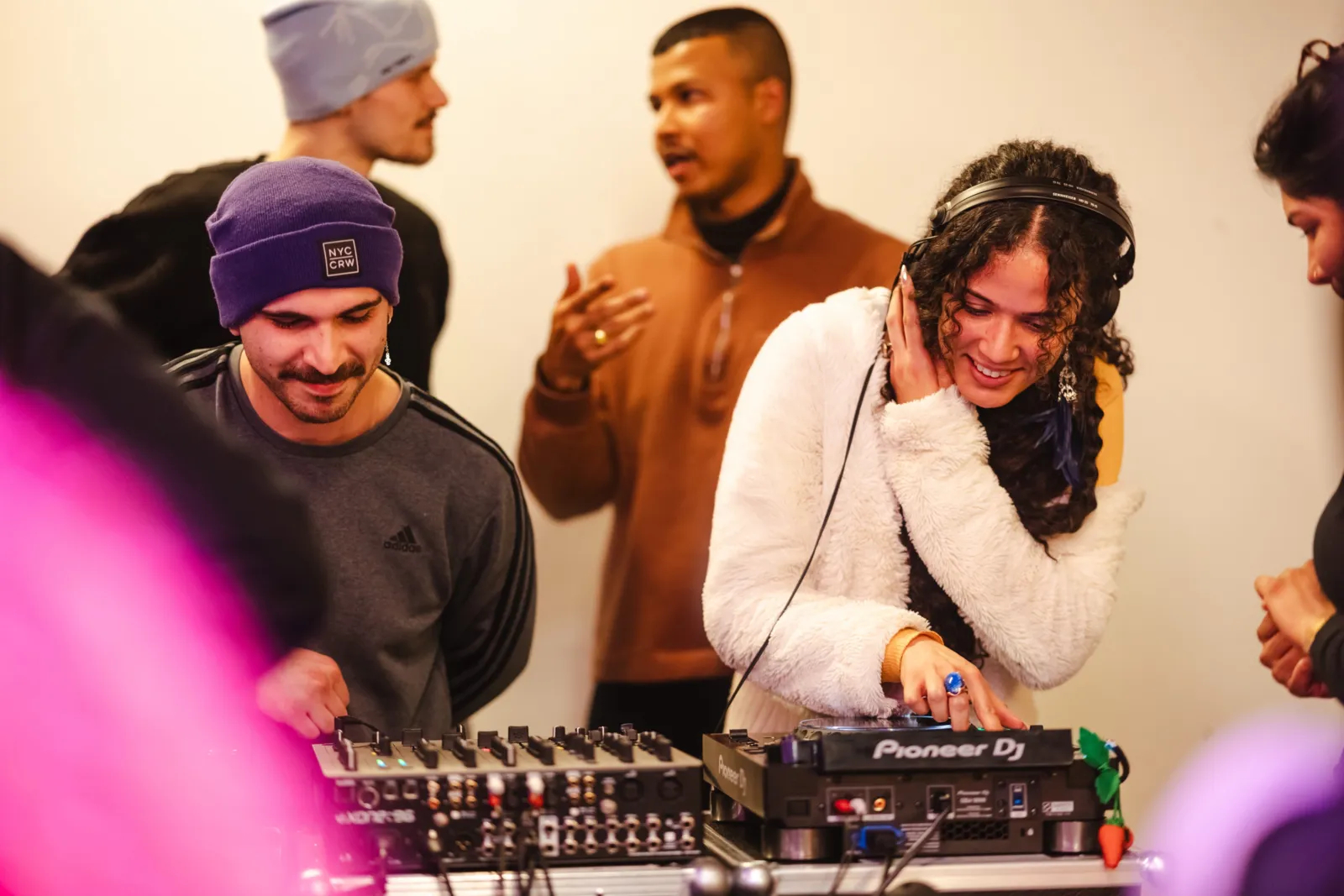 F&uuml;nf Personen. Zwei stehen an einem DJ-Pult. Zwei Personen im Hintergrund unterhalten sich. Eine Person ist nur halb am rechten Bildrand zu sehen.