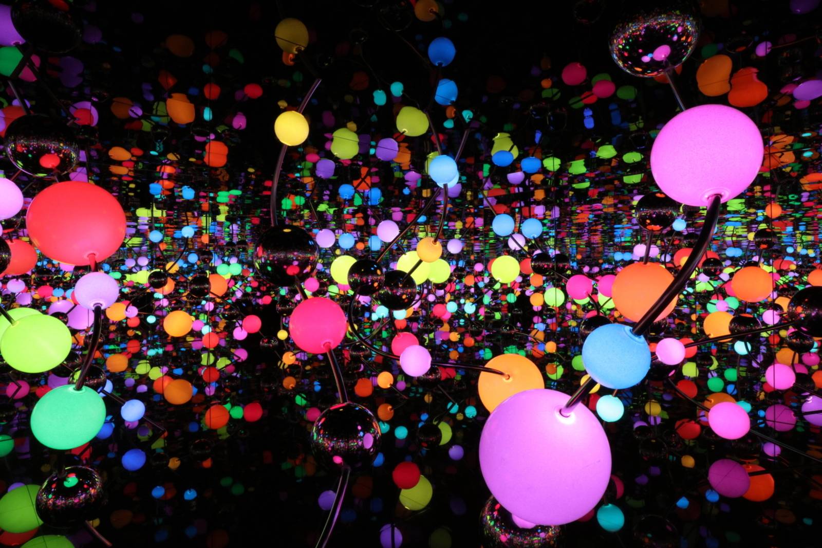 Zu sehen ist eine Lichtinstallation von Yayoi Kusama. Bunt leuchtende Kungeln in unterschiedlichen Farben sind in einem dunklen aber spiegelnden Raum verteilt.