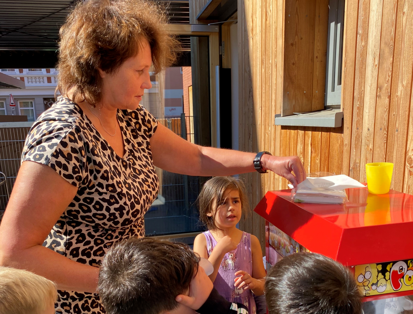 Dezernentin Rita Maria Ryski steht mit Kindern an einer Popcornmaschine und gibt Popcorn an die Kinder aus.