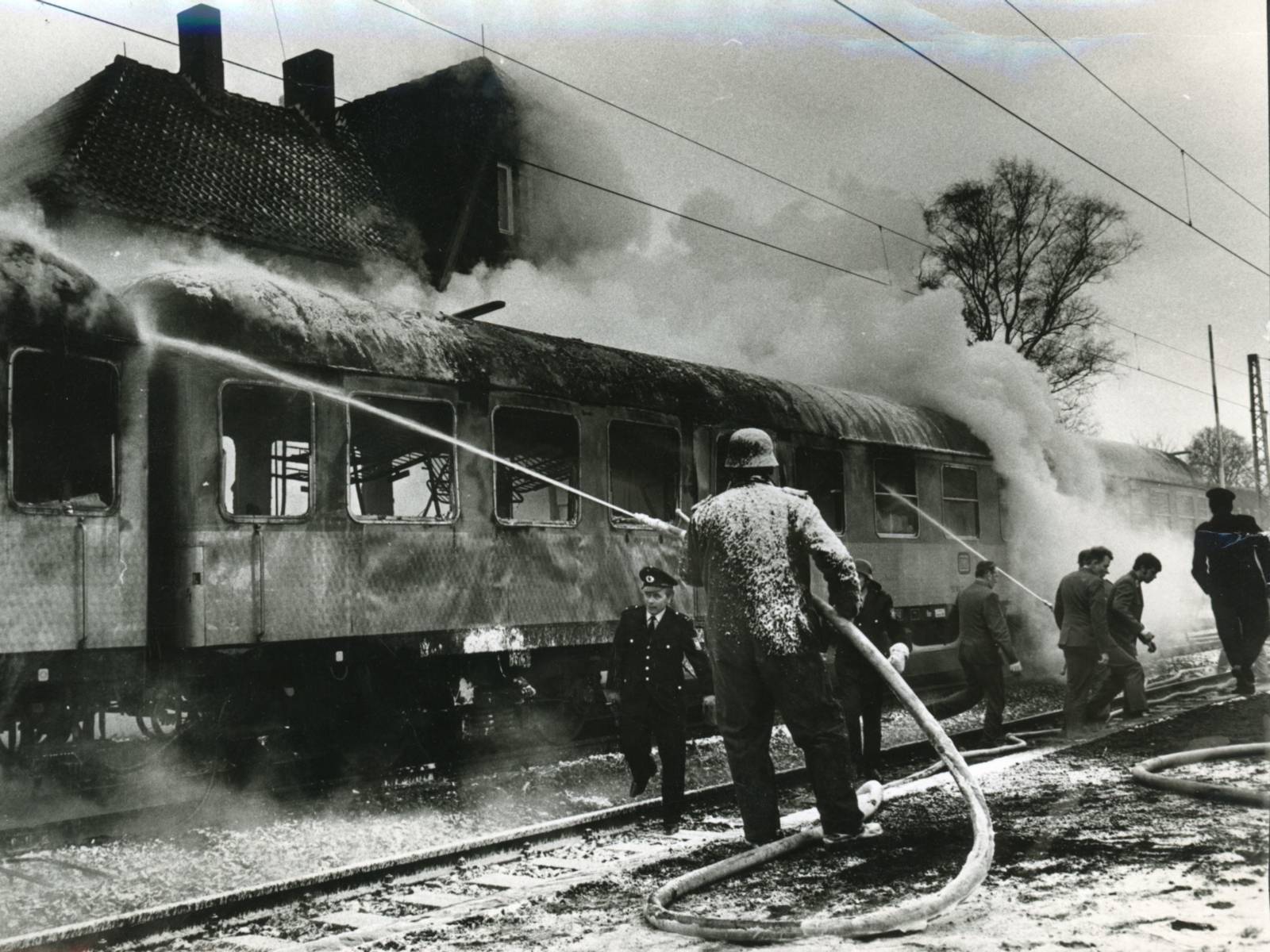 Historisches Schwarz-Weiß-Foto: Feuerwehrleute löschen einen Personenwaggon.