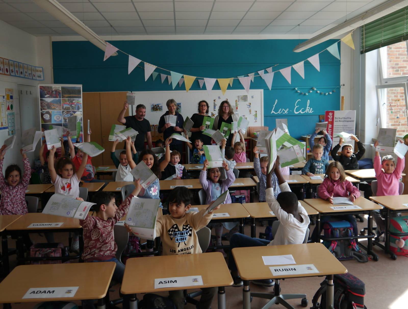 Kinder in einer Klasse halten Schulhefte in die Luft.