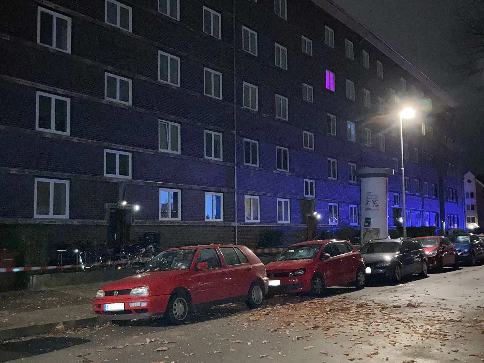 Eine Häuserreihe im Hintergrund, auf der Straße davor parken Autos, auf der Straße liegen Dachziegel