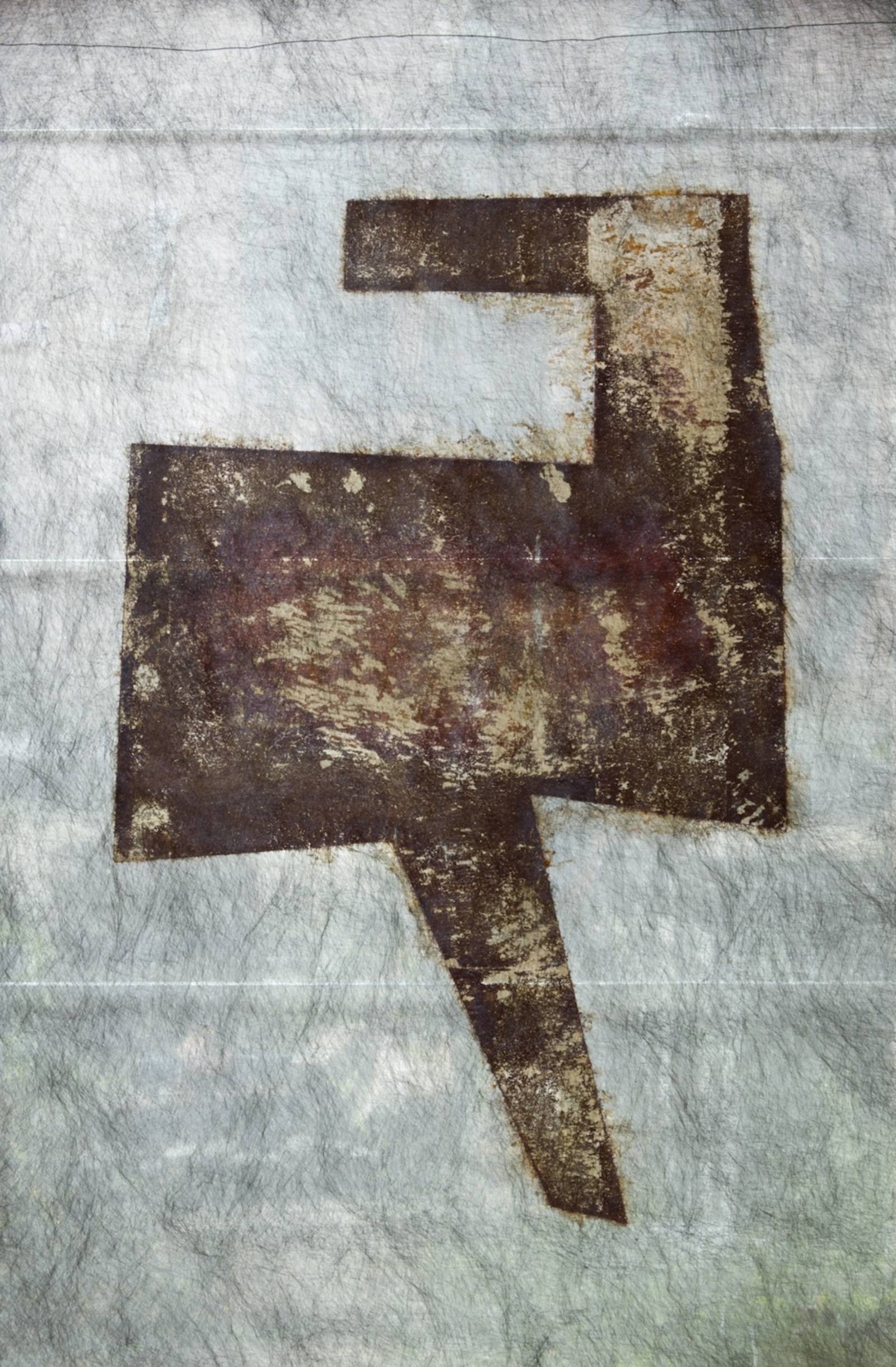 Zu sehen ist eine grafische Arbeit von Hartmut Stielow. Hier ist mithilfe eines chemischen Prozesses ein Druck aus Rost auf ein Vlies übertragen worden. Der Druck zeigt eine hartkantige, geometrische Figur.