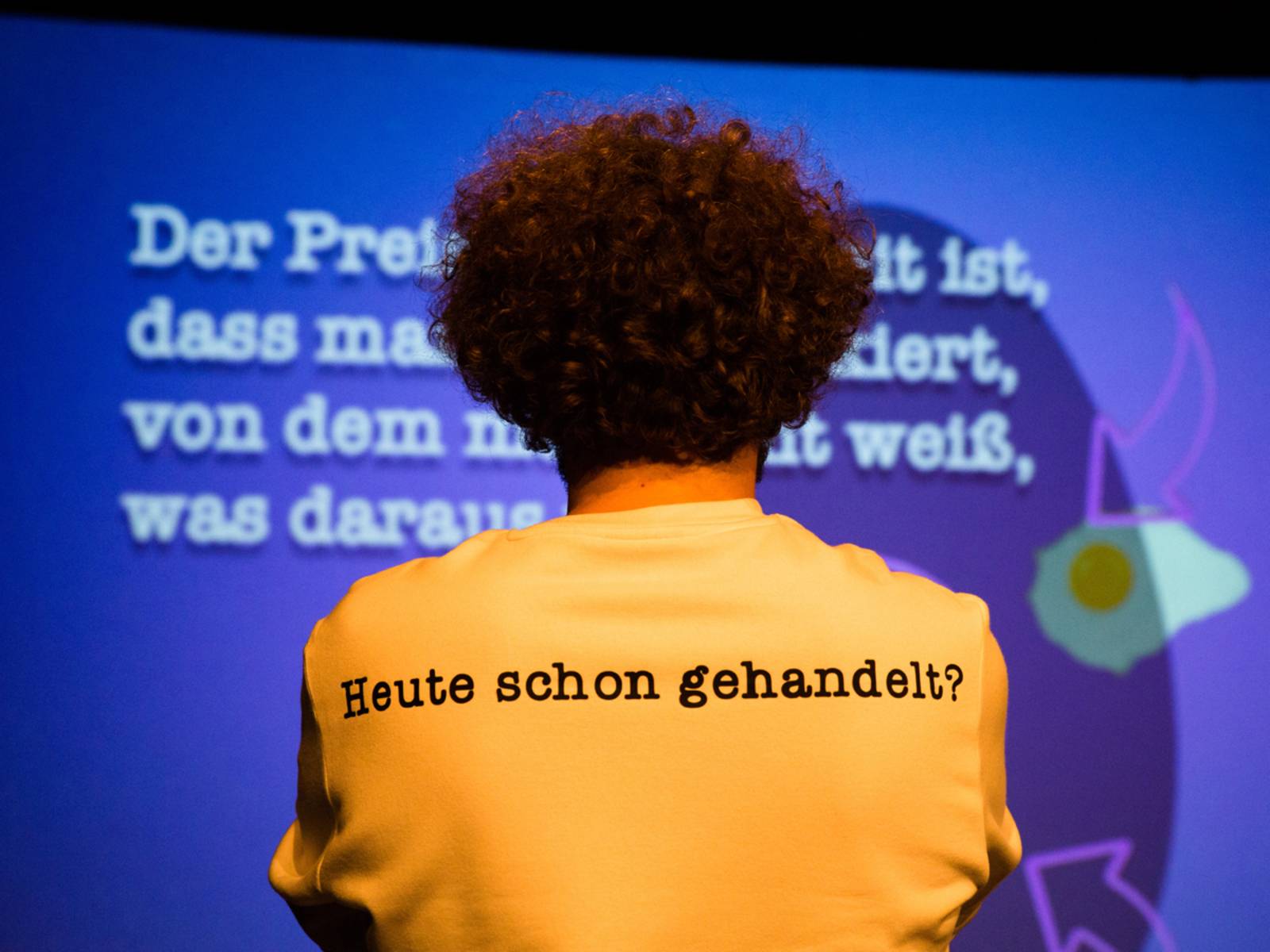 Eine Person steht mit dem Rücken zum Betrachter, auf dem Rücken des T-Shirts steht "Heute schon gehandelt?".