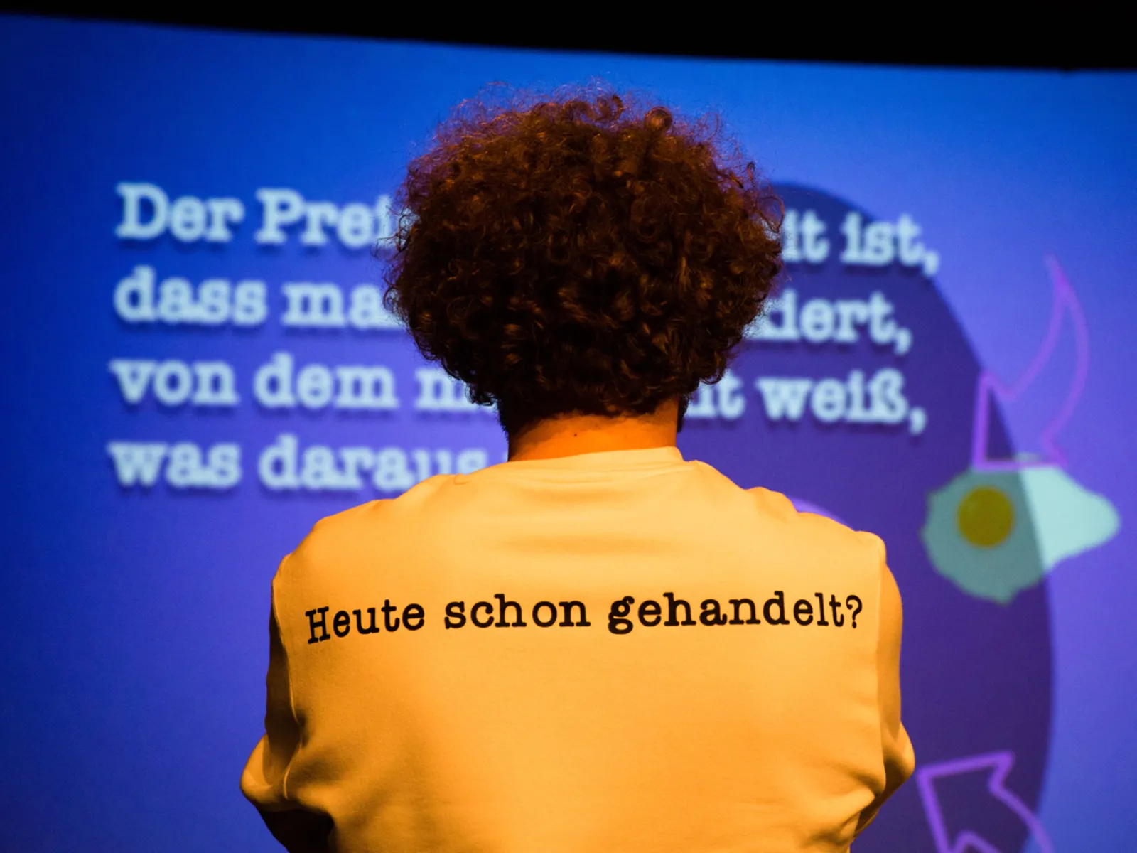 Eine Person steht mit dem Rücken zum Betrachter, auf dem Rücken des T-Shirts steht "Heute schon gehandelt?".