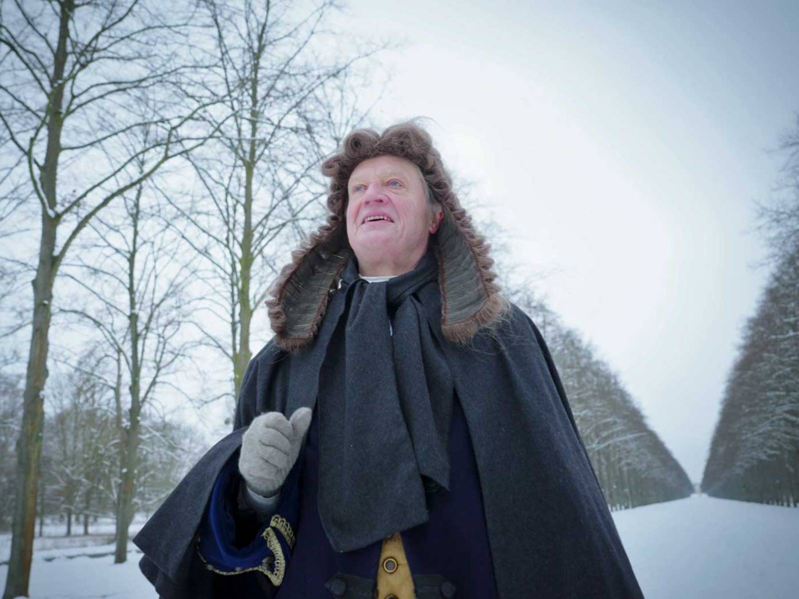 Mann mit historischer Perücke in verschneiter Allee.