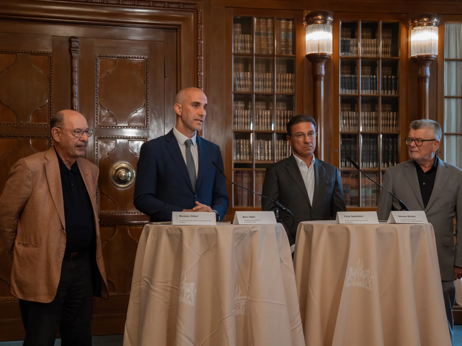 Vier Männer bei einem Pressegespräch. Sie stehen an Tischen.