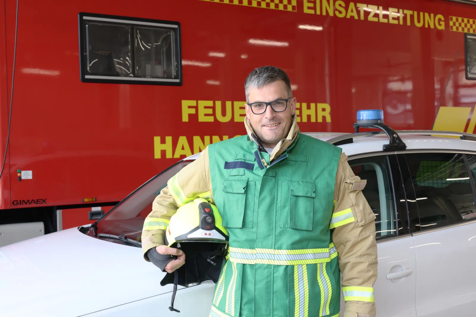 Pressesprecher mit gr&uuml;ner Weste vor dem Einsatzleitwagen 3-4