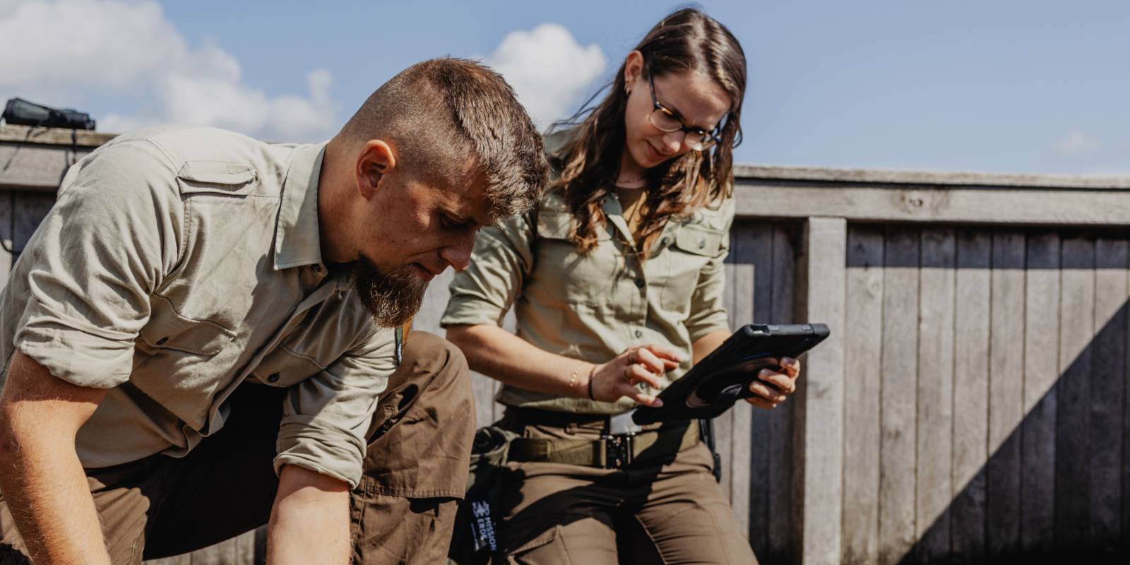 Eine Rangerin und ein Ranger knien auf einem Holzboden und begutachten die groben Dielen.