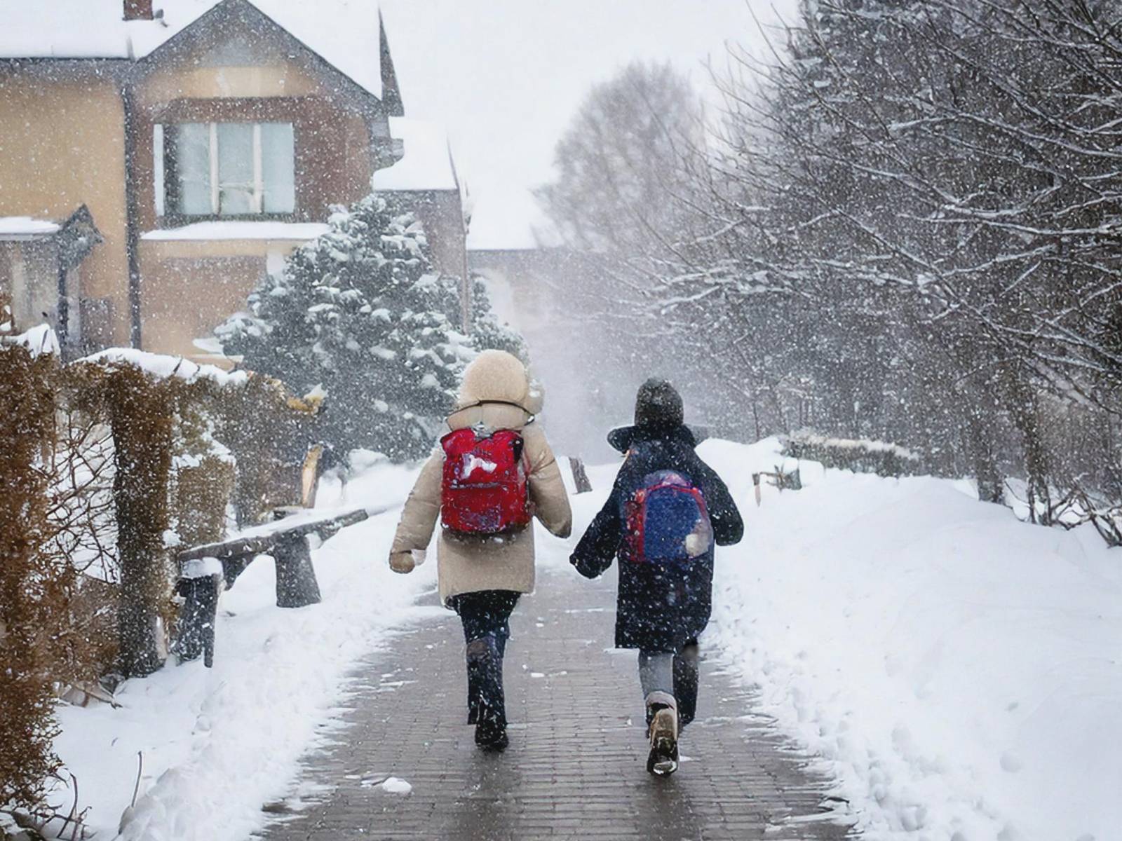 Zwei Kinder laufen auf einem Weg, umsäumt von Schnee und Häusern im Schneegestöber.