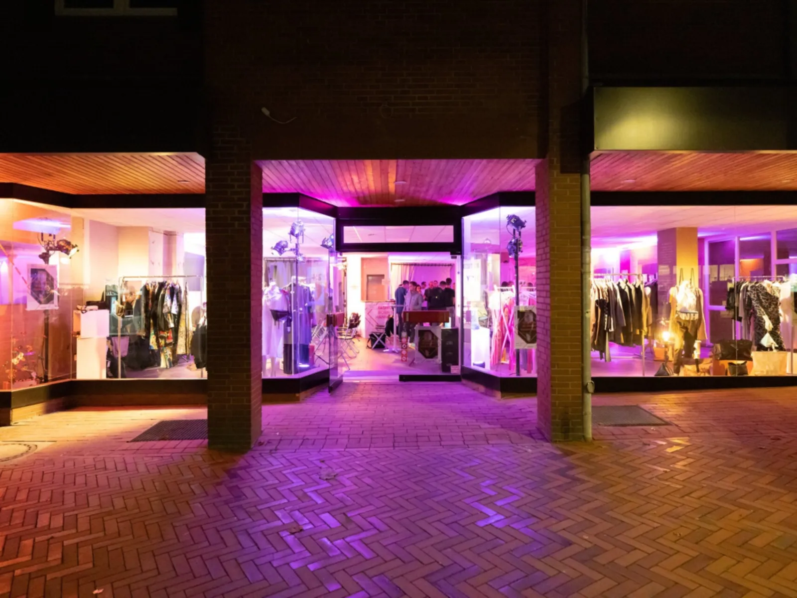 Eine Schaufensterzeile bei Nacht in lila Neonlicht. Im Ladengeschäft sind hauptsächlich Kleidungsstücke zu sehen.