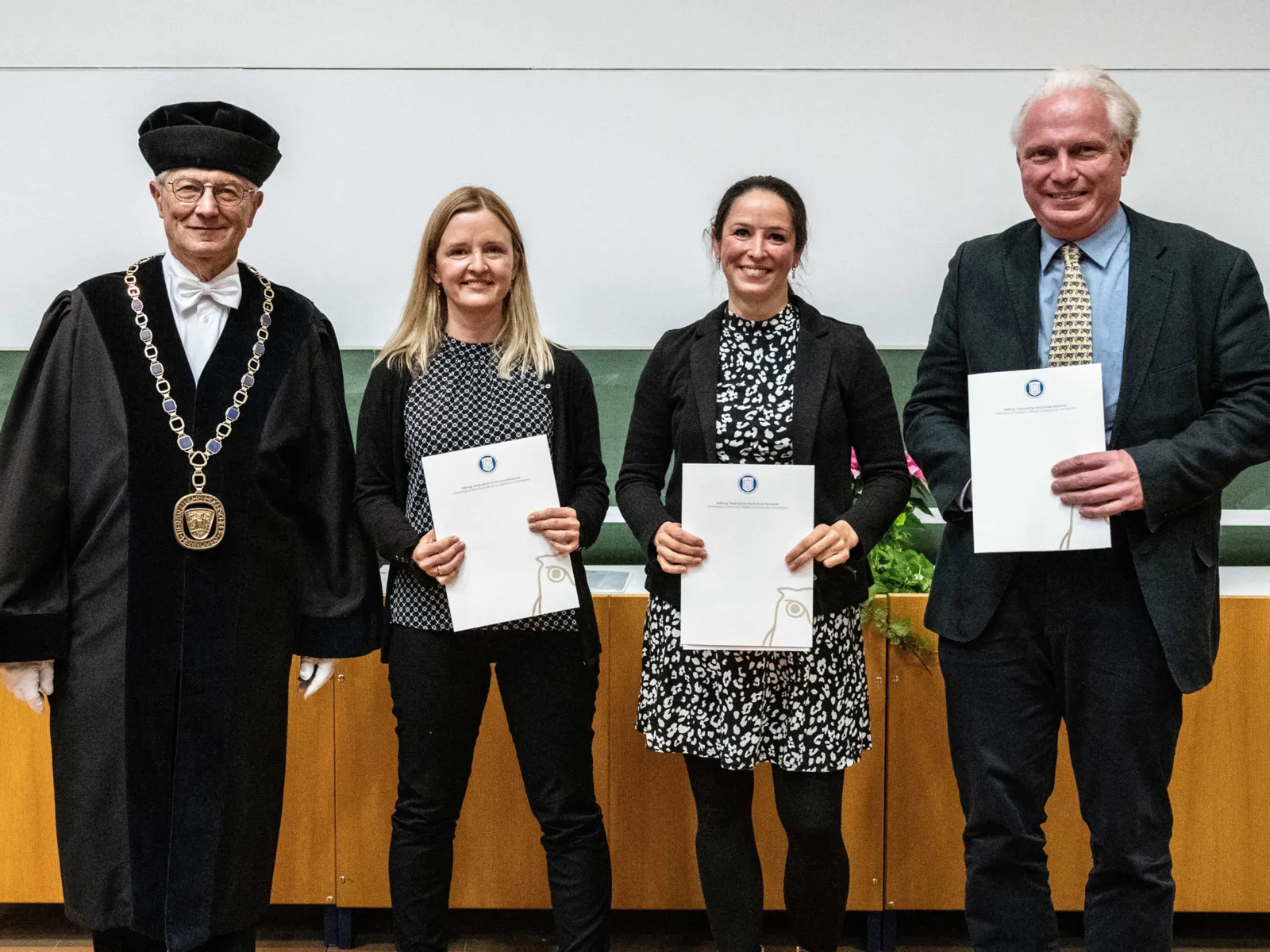 Zwei Frauen und zwei M&auml;nner, die Frauen und einer der M&auml;nner halten Urkunden in den H&auml;nden, der zweite Mann tr&auml;gt ein festliches Ornat.
