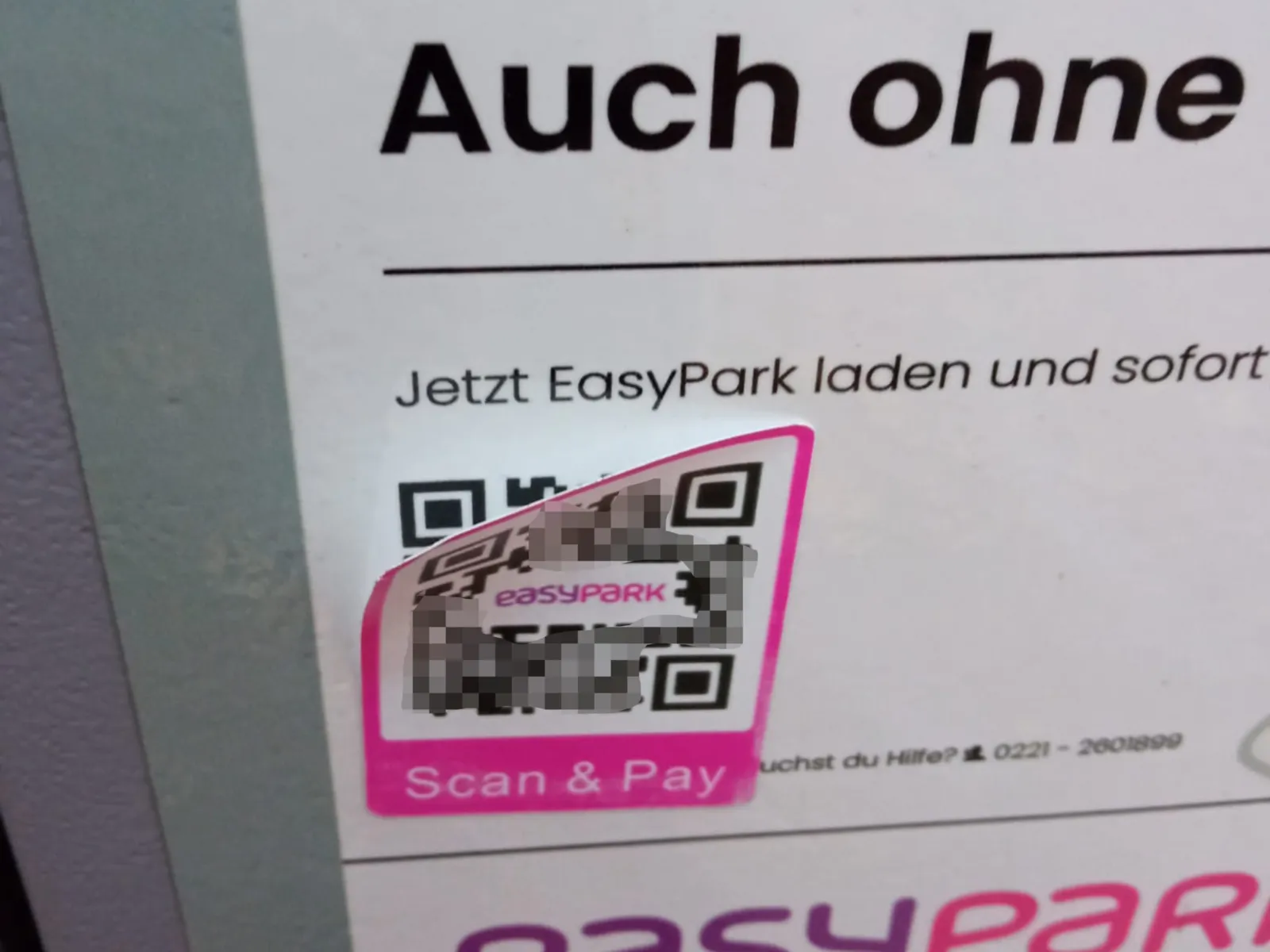 Ein Aufkleber mit einem pink umrandeten QR-Code über einem schwarz-weißem QR-Code ist an der oberen Ecke leicht gelöst. In der Mitte steht easypark, darunter Scan & Pay.