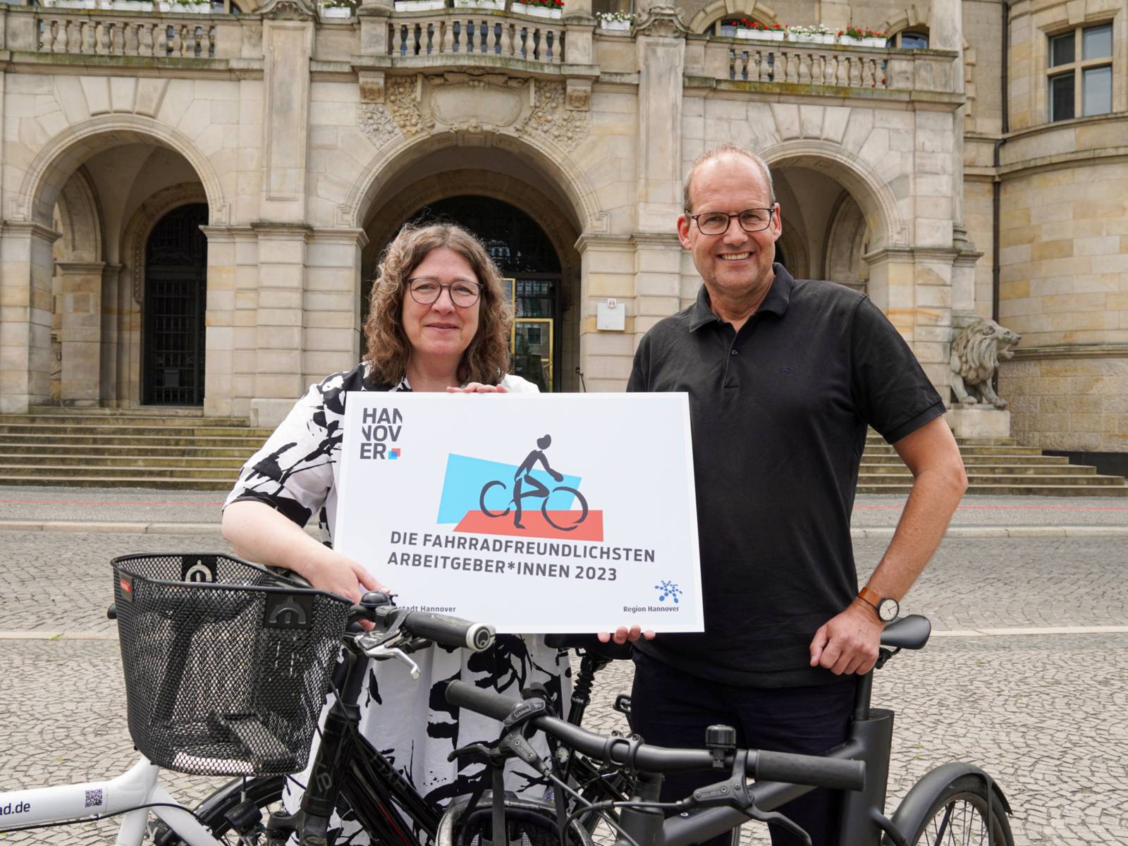 Zwei Personen an einem Fahrrad. Sie halten ein Schild, auf dem "Die Fahrradfreundlichsten Arbeitgeber*innen 2023" steht.