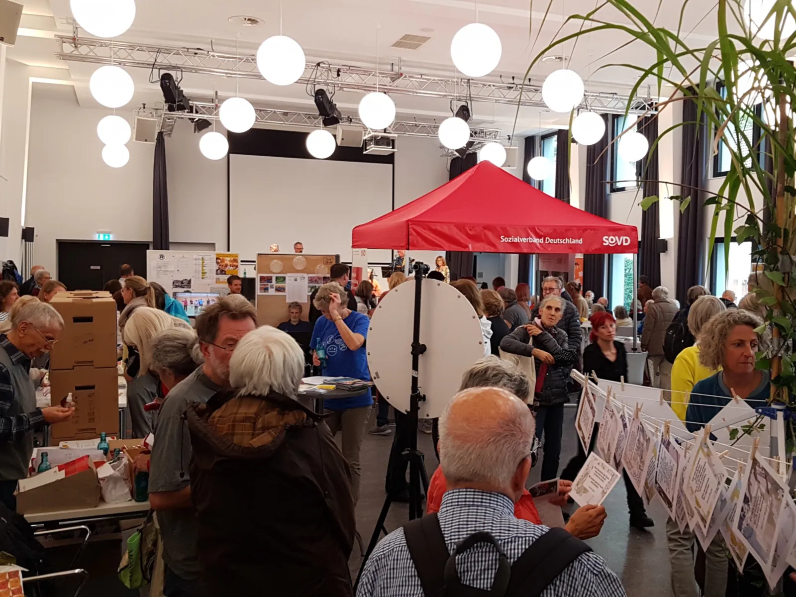 In einem Saal stehen Menschen an Ständen, laufen umher oder unterhalten sich.