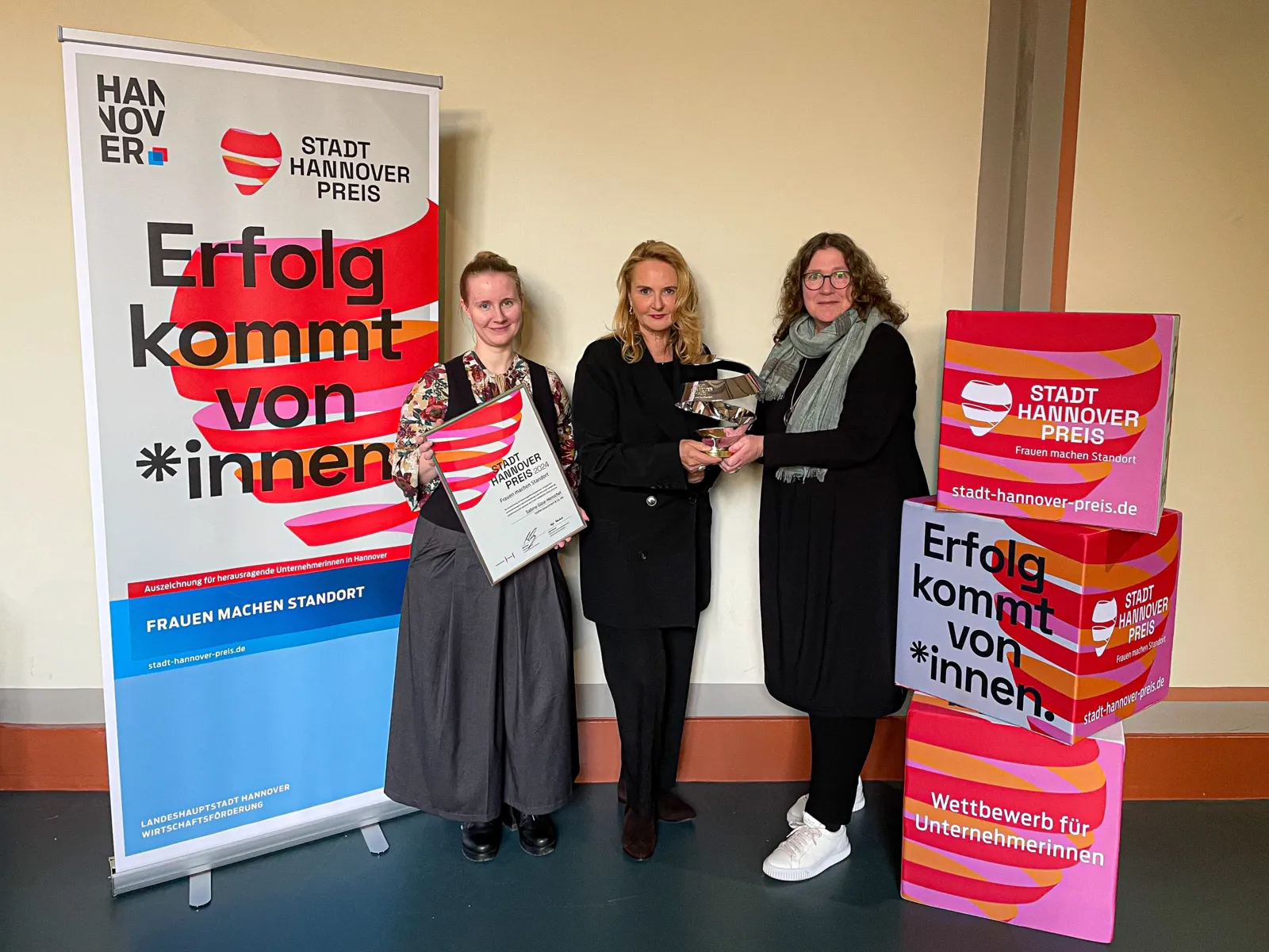 Drei Personen zwischen Aufstellern zum Stadt-Hannover-Preis.