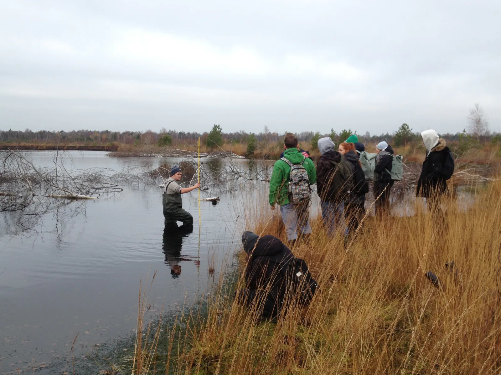 Eine Person in Watthose im Wasser, andere Personen stehen am Uferrand