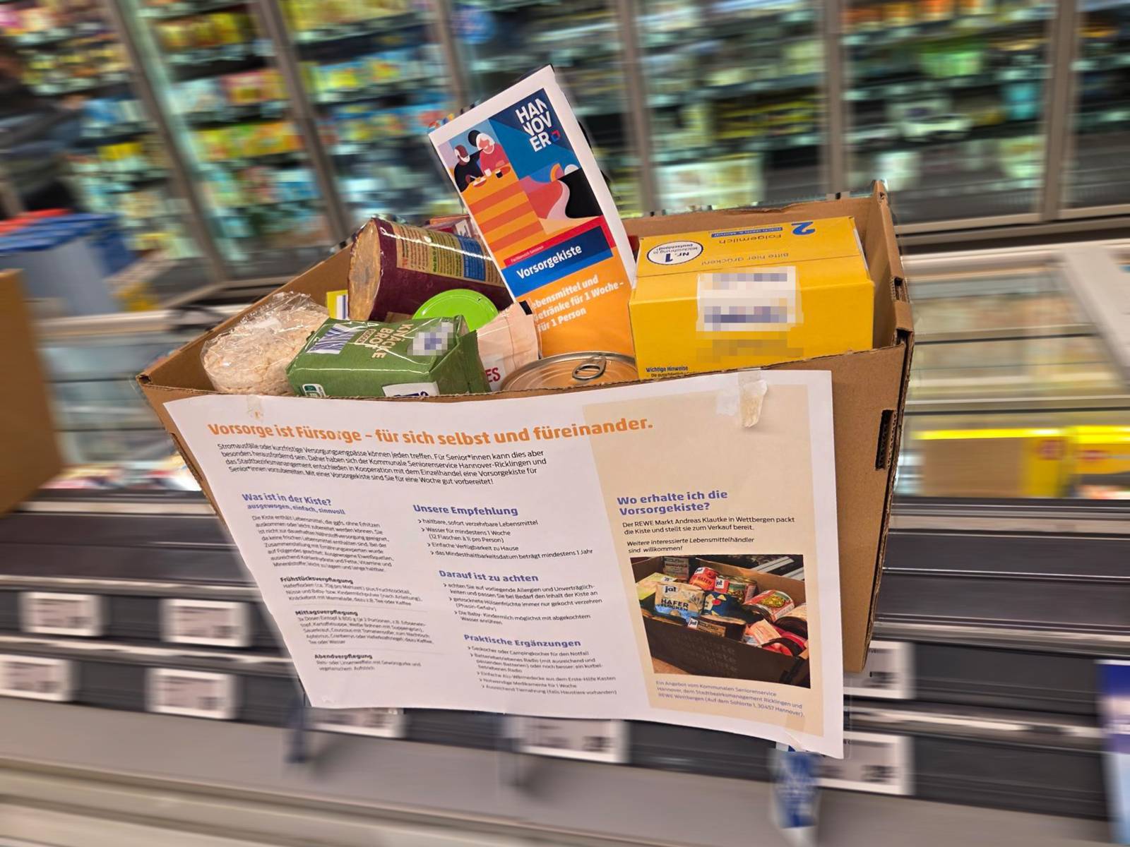 Ein Karton mit Lebensmittelpackungen steht in einem Supermarkt auf einer Kühltruhe.