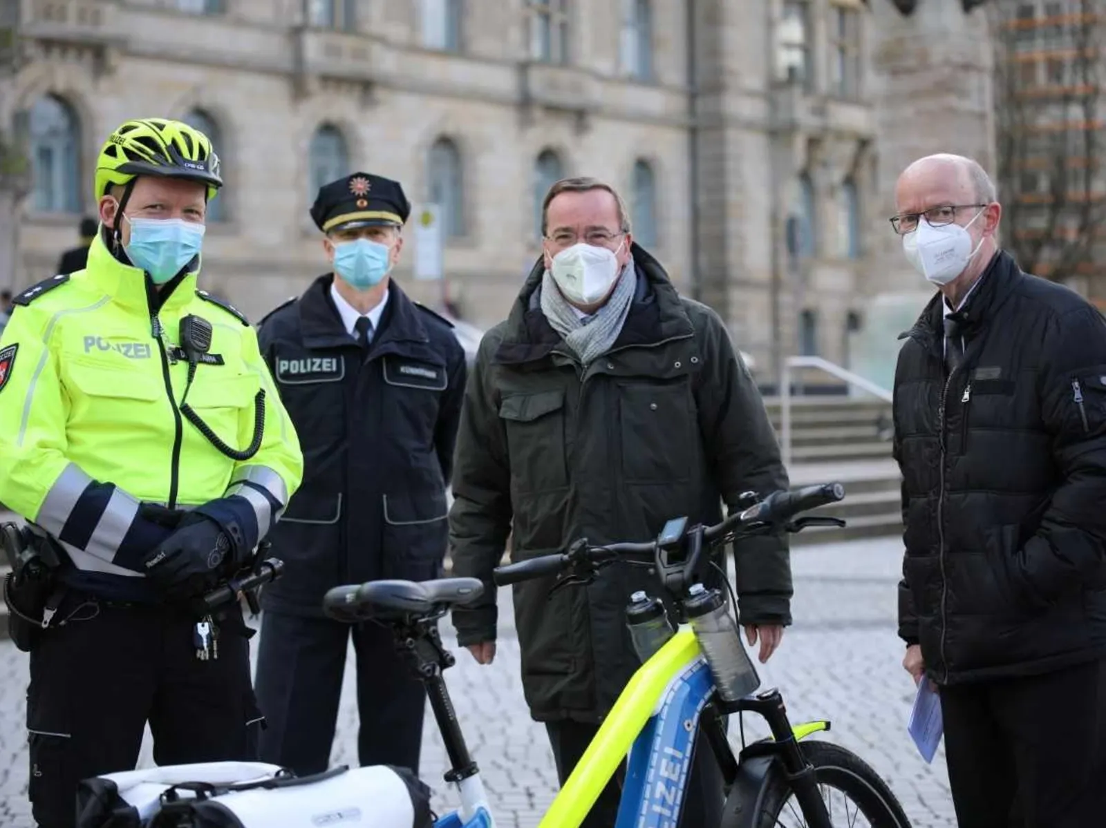 Zwei Männer in Polizeiuniformen und zwei Männer in Anzügen stehen hinter einem Fahrrad.