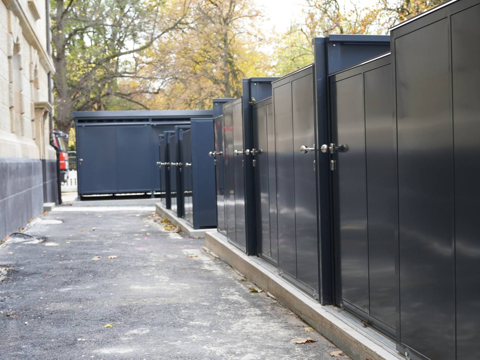 Links eine Gebäudewand, rechts schwarze Metalltüren, dazwischen ein Gang.