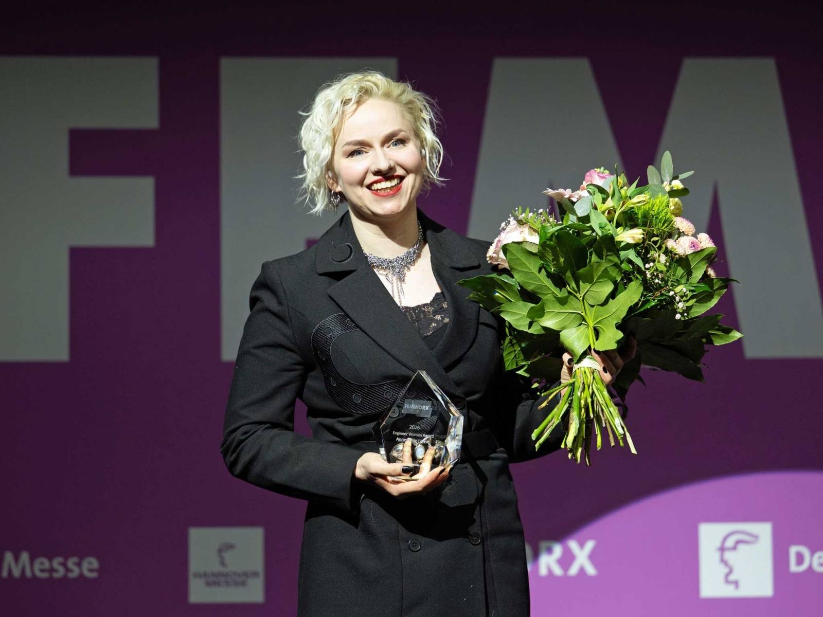 Eine Frau mit Blumenstrauß und Preis aus Kristall.