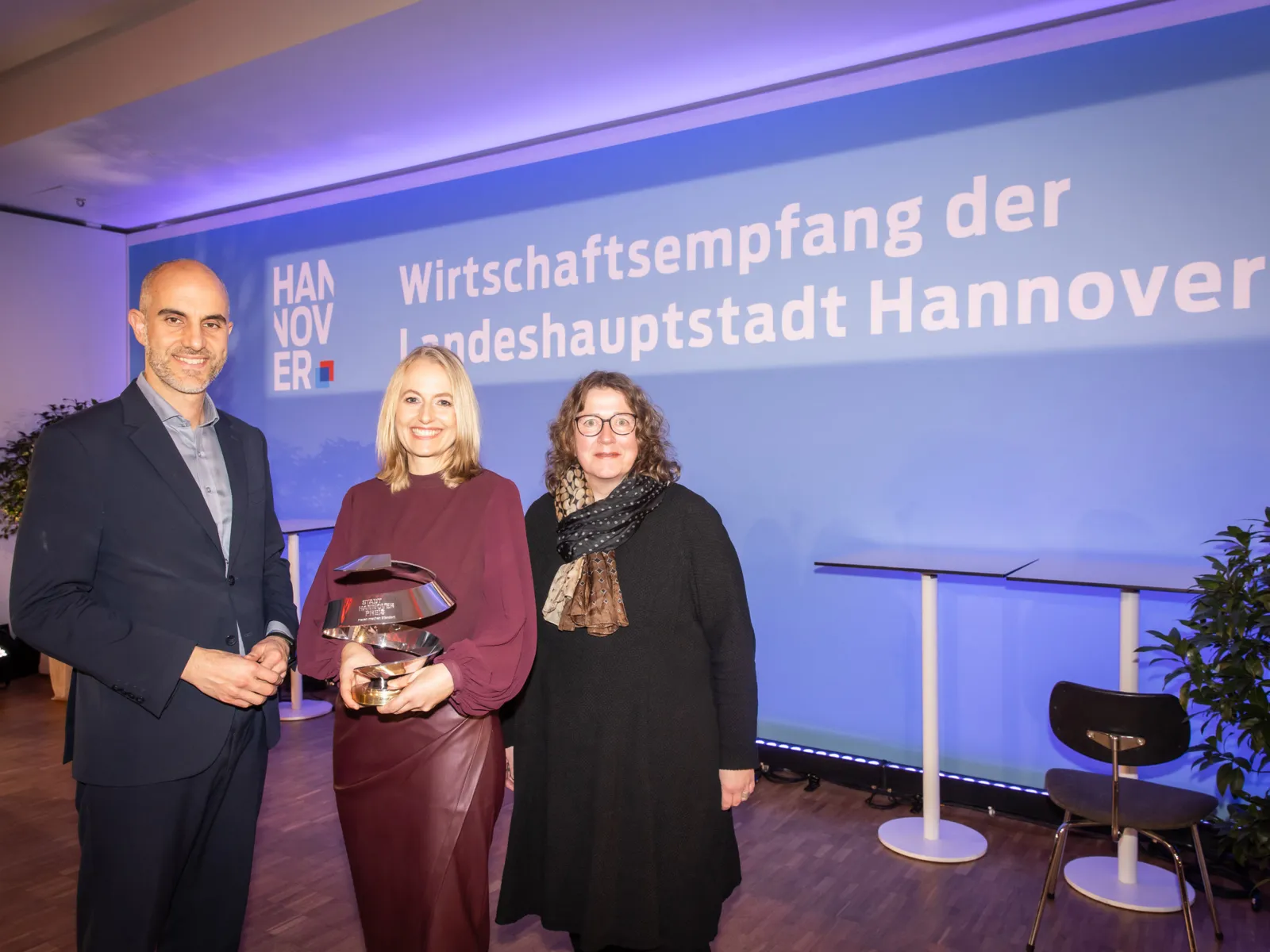 Drei Personen auf einer Bühne. Eine hält einen Preis in den Händen.